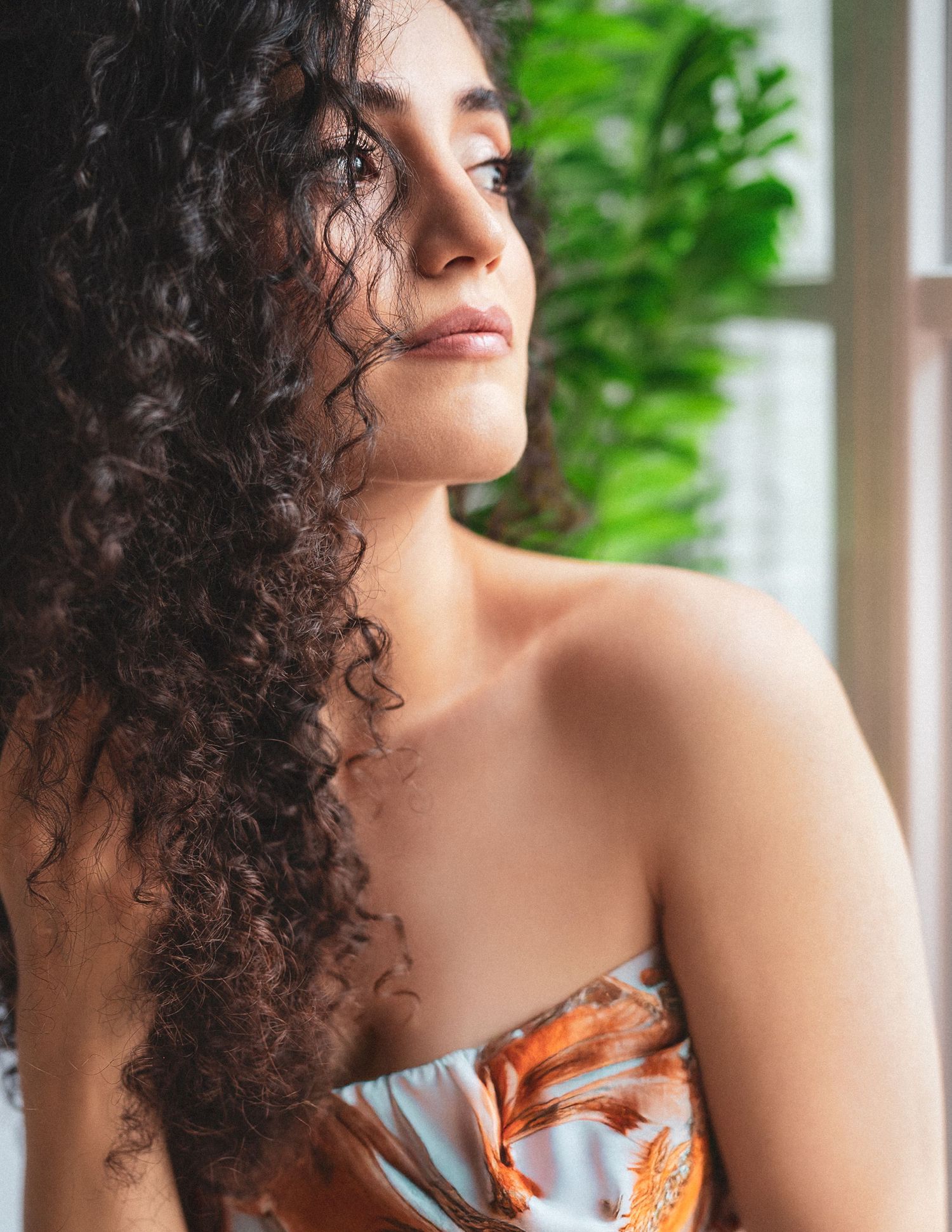 Elegant portrait with curly hair and bare shoulders against a green background.