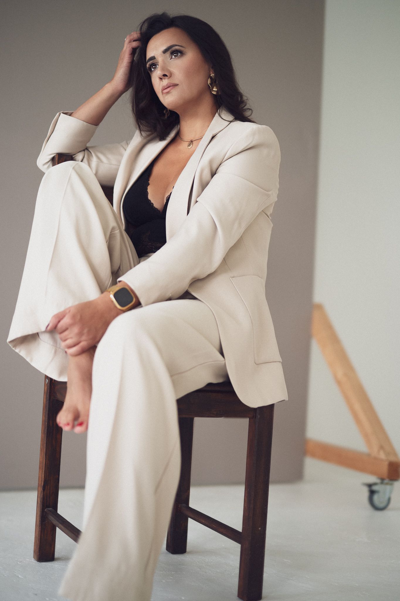 Fashion editorial with cream suit and wooden chair in studio setting.