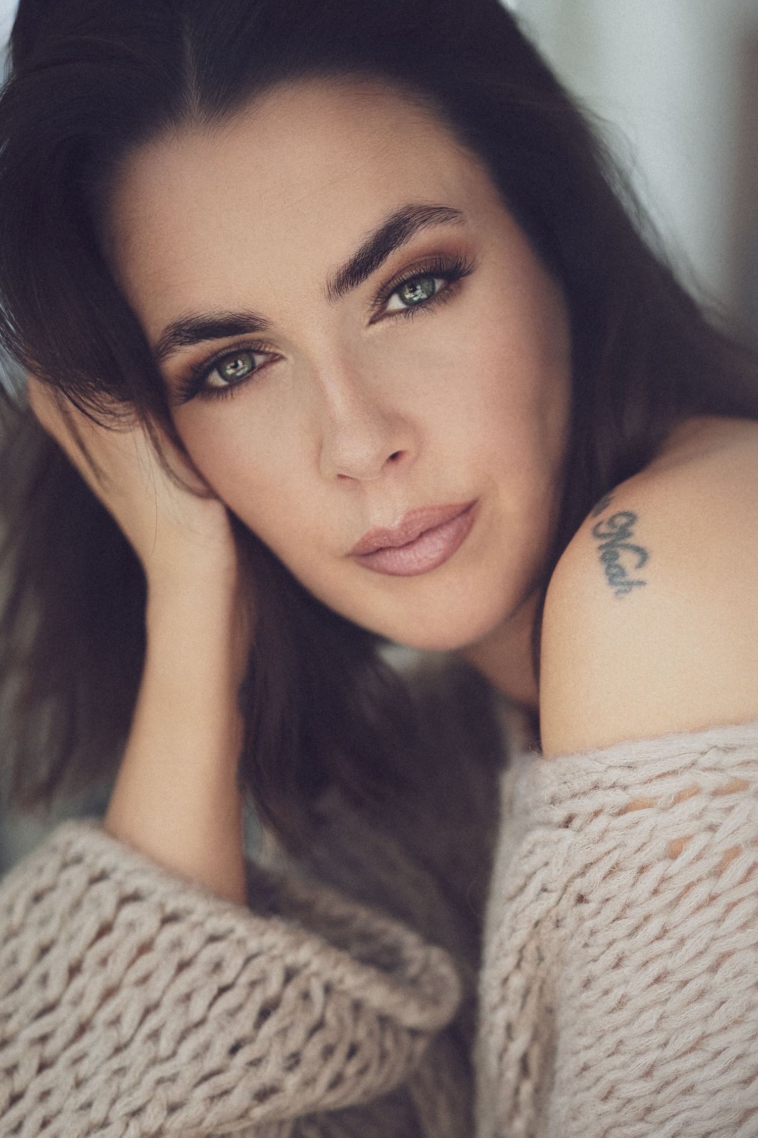 Portrait photo of someone wearing a cozy beige knit sweater in soft lighting with visible tattoo details.