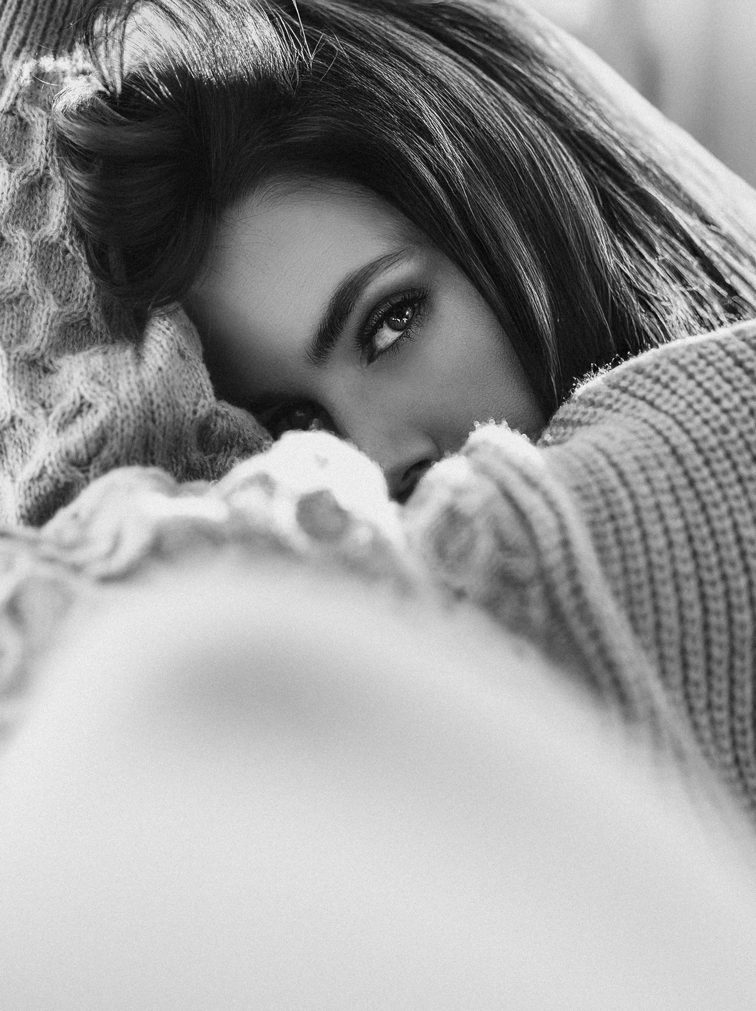 A series of black and white portraits showing a person lying down with dark hair against a soft sweater background.