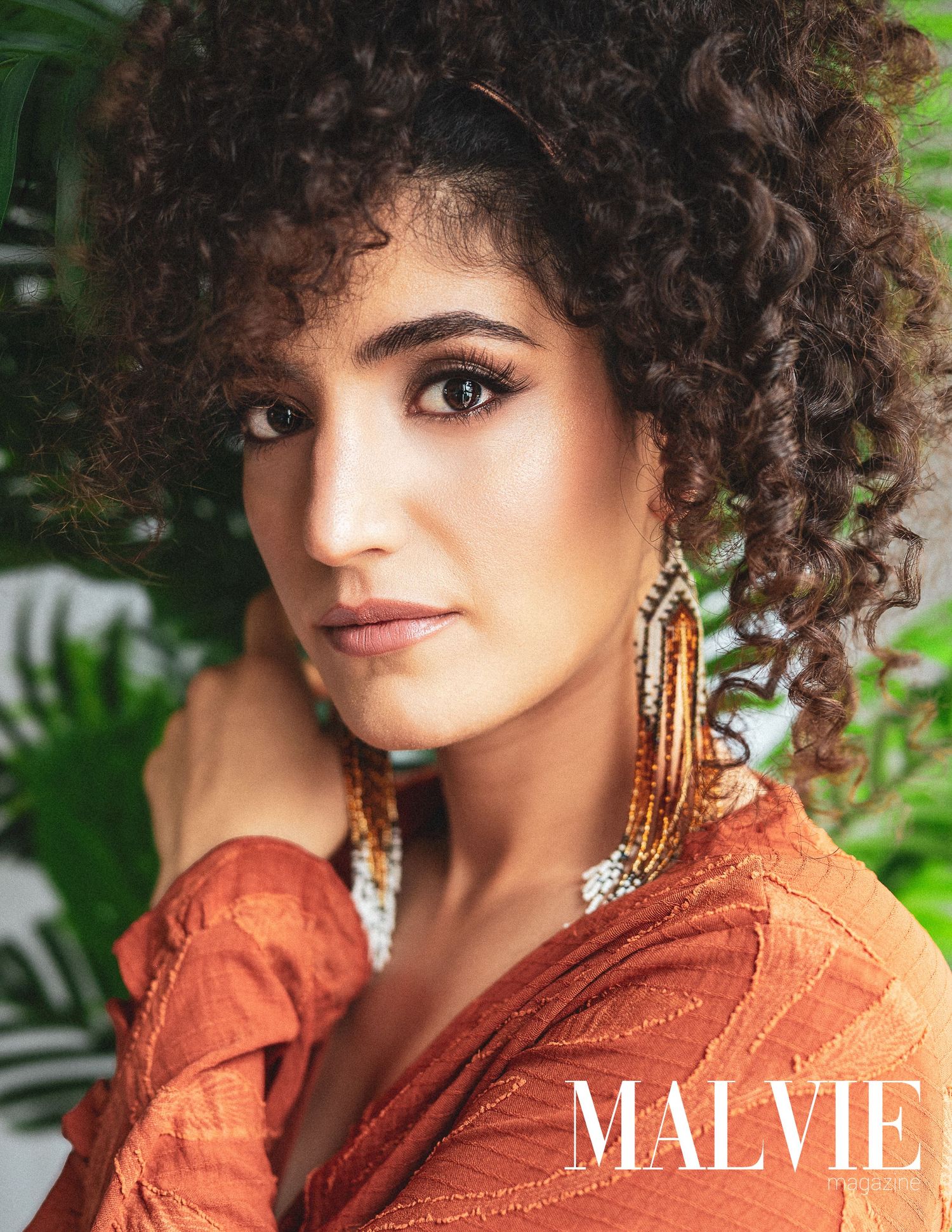 Woman with curly hair wearing orange top and beaded earrings on MALVIE magazine cover.