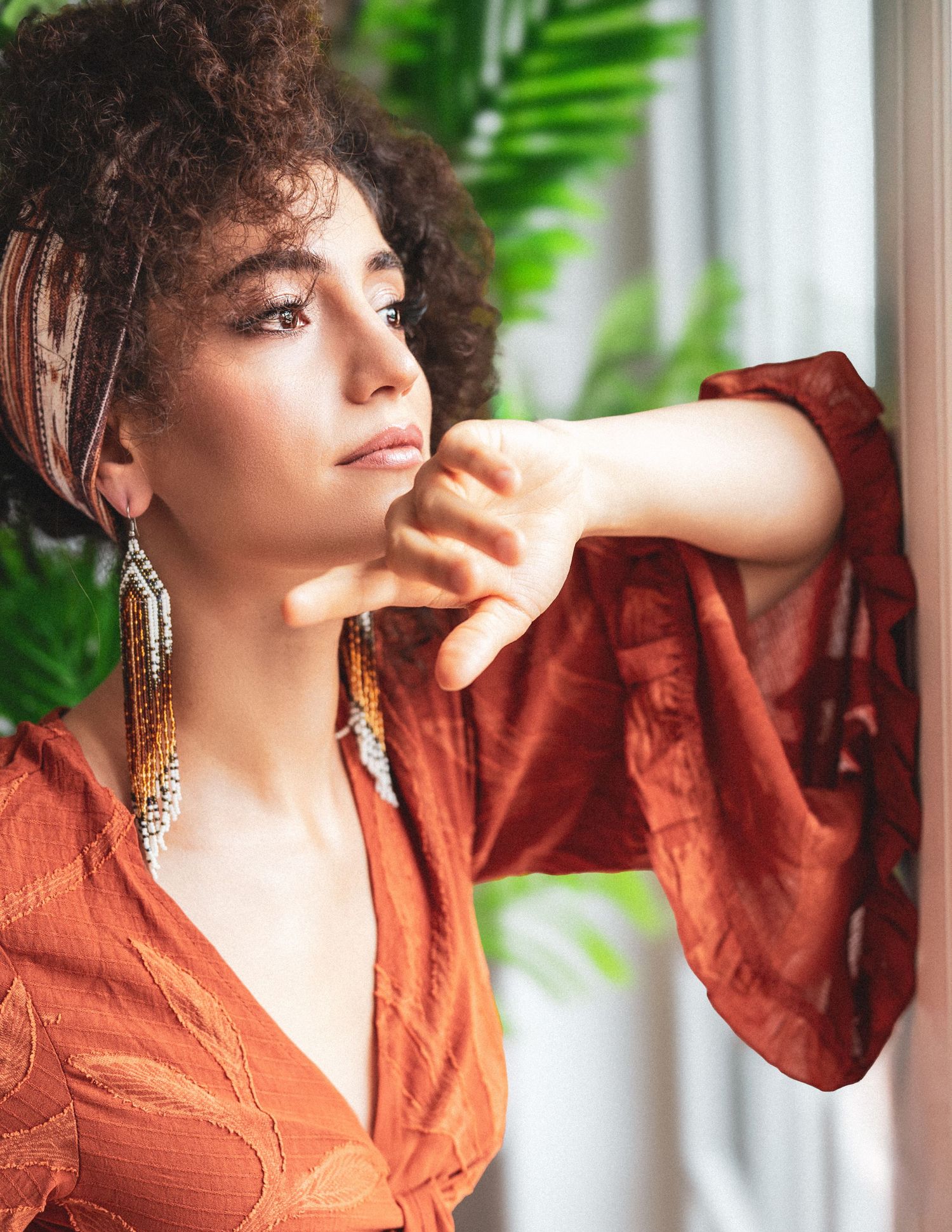 Fashion series in a rust-colored blouse with natural curls and statement jewelry.