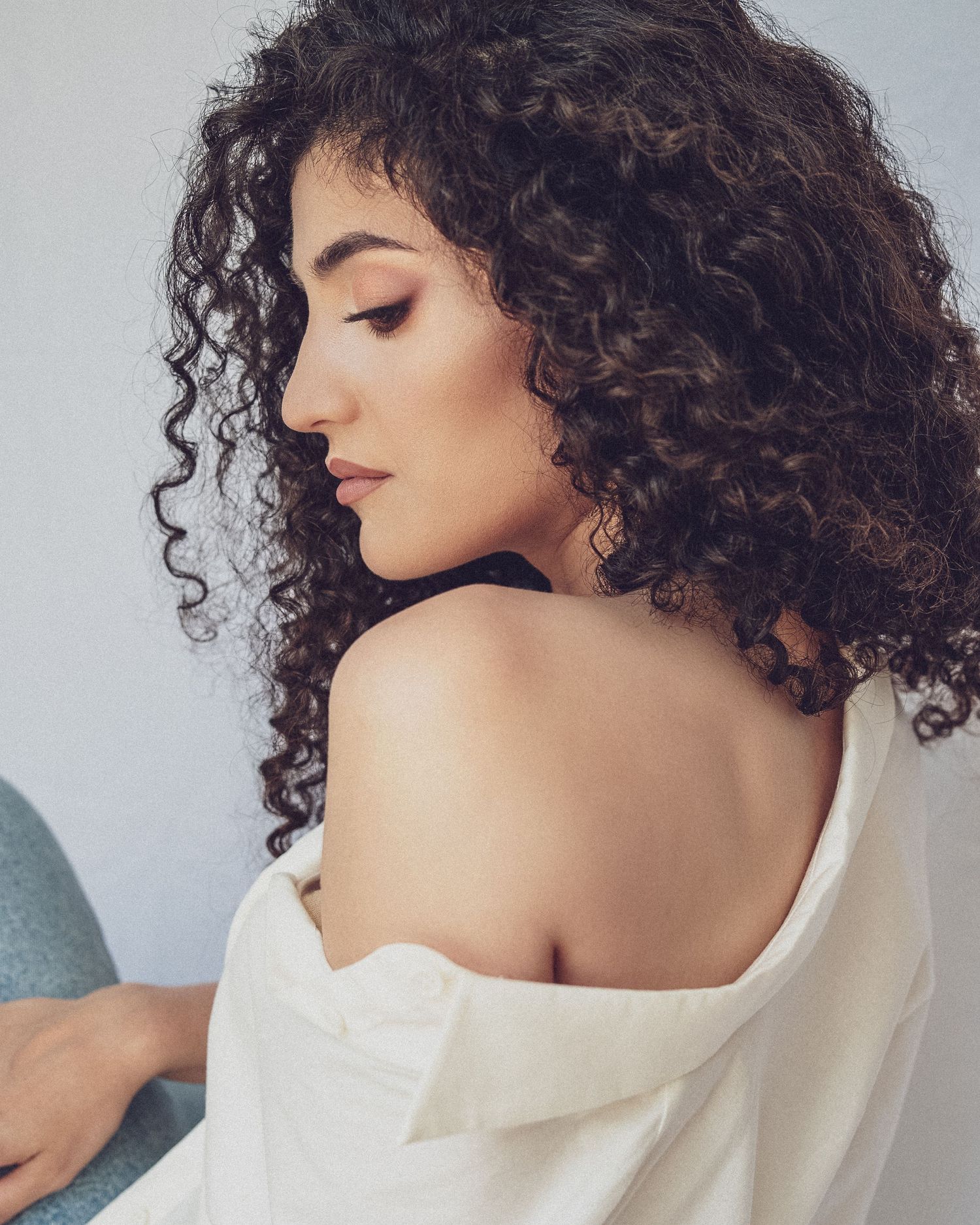 Artistic portrait series featuring white off-shoulder top and natural curly hair against light background.