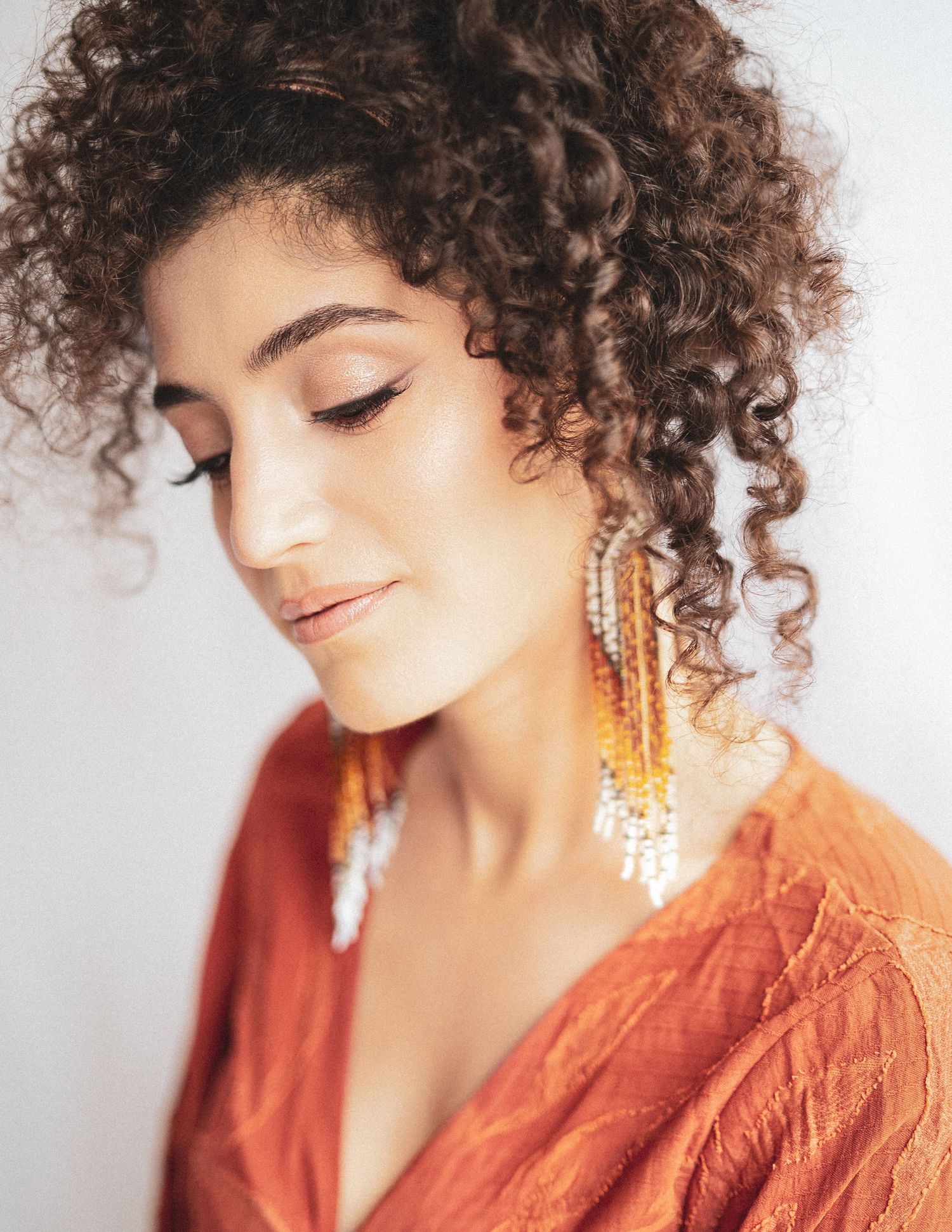 Artistic portrait with natural curly hair and statement earrings in warm orange tones.