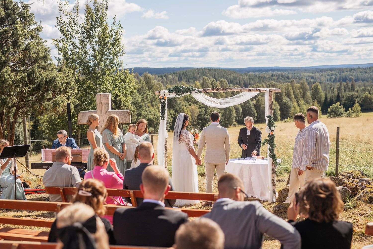 Bröllops i naturen, bland kossor, gräs, bröllopsbågar, bänkar fyllda med gäster, bröllopsfotograf Jennifer serrander