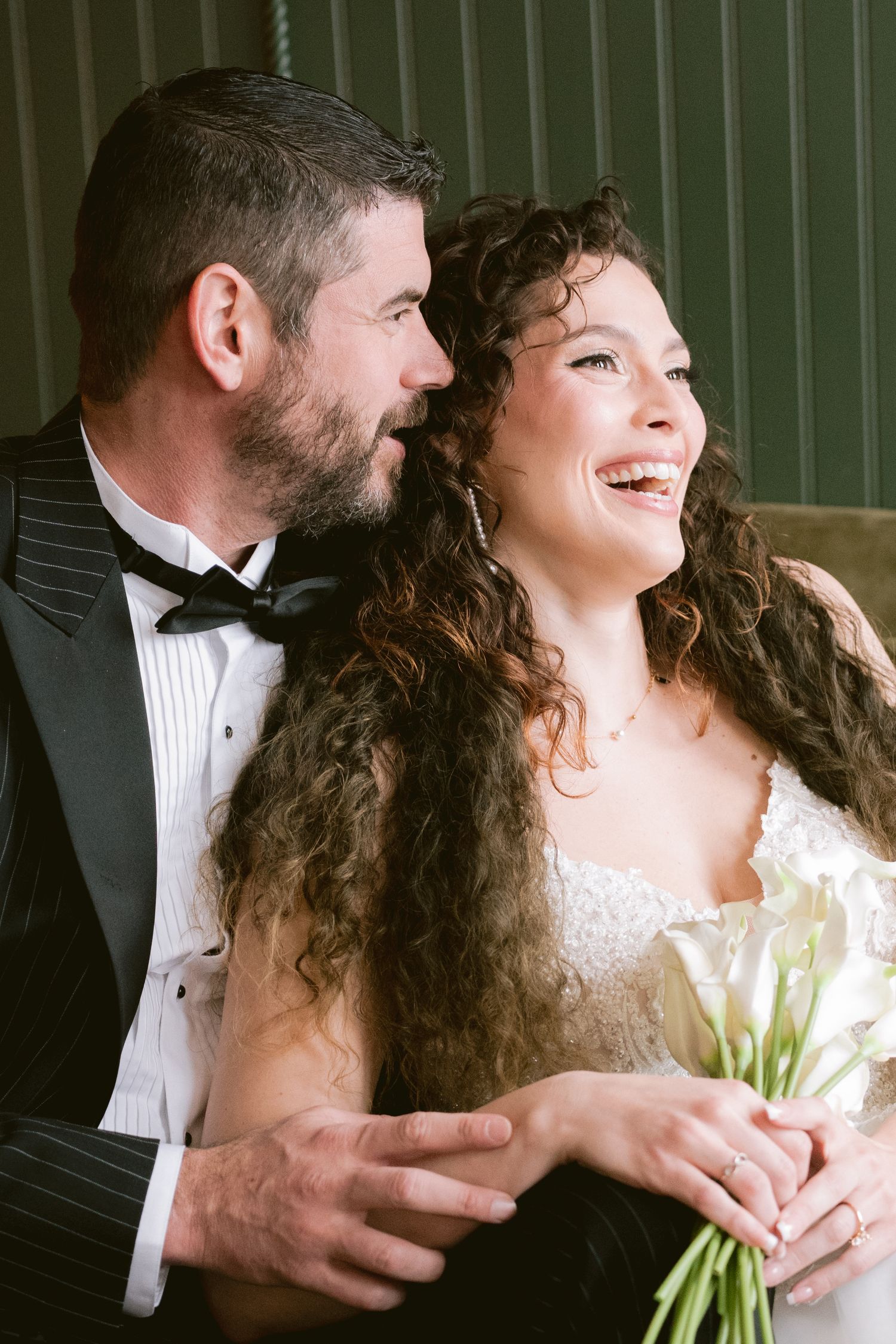 A bride and groom posing on a velvet couch and laughing