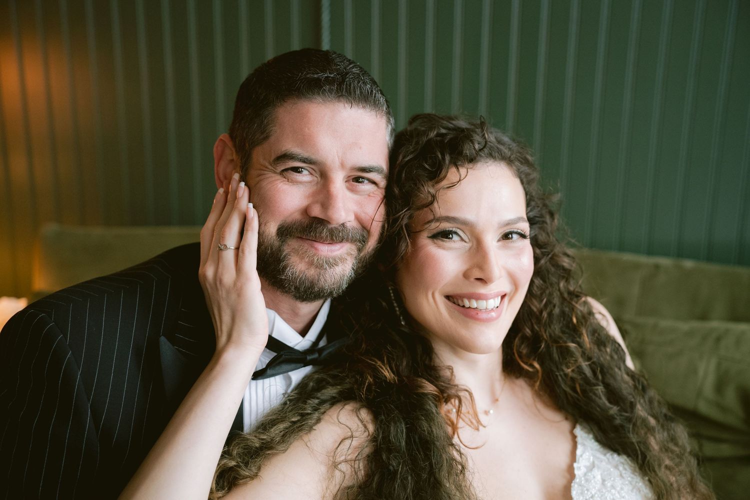 A bride and groom posing on a velvet couch and laughing