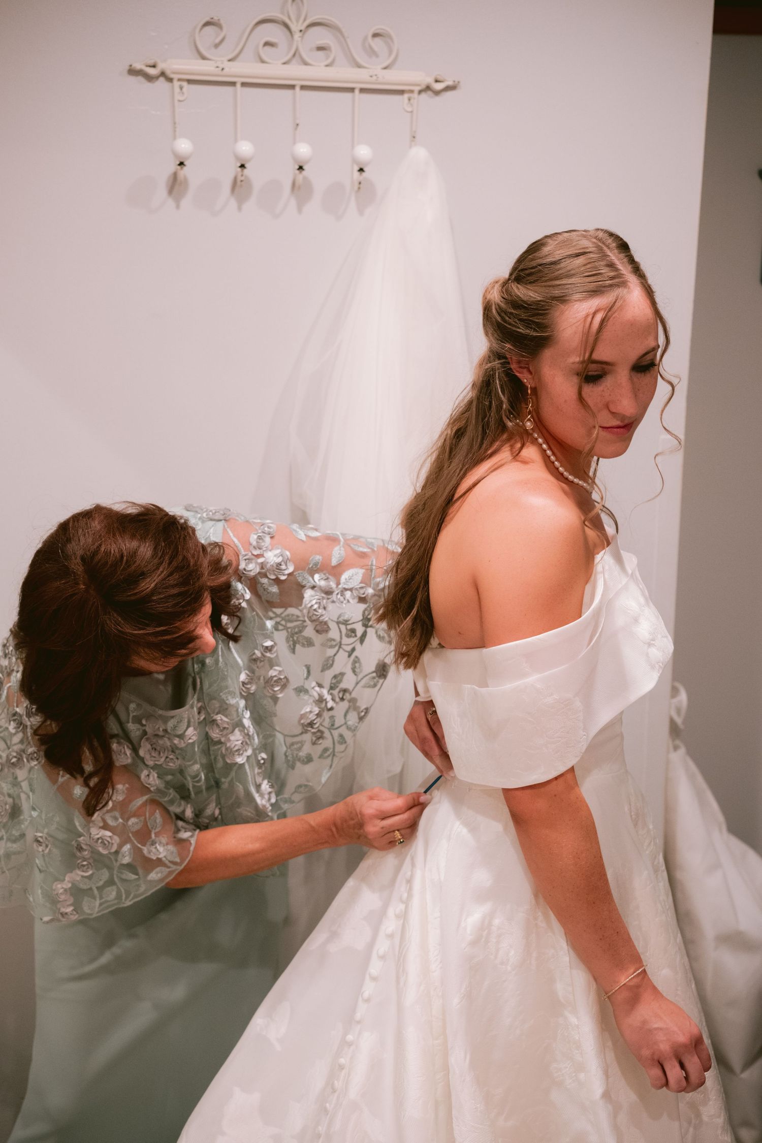 A mom helping her daughter, a bride, fix her dress