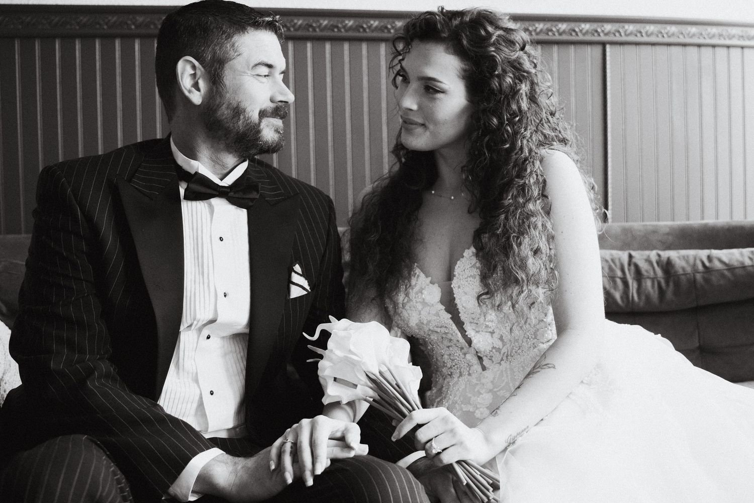 A bride and groom smiling at each other on a velvet couch