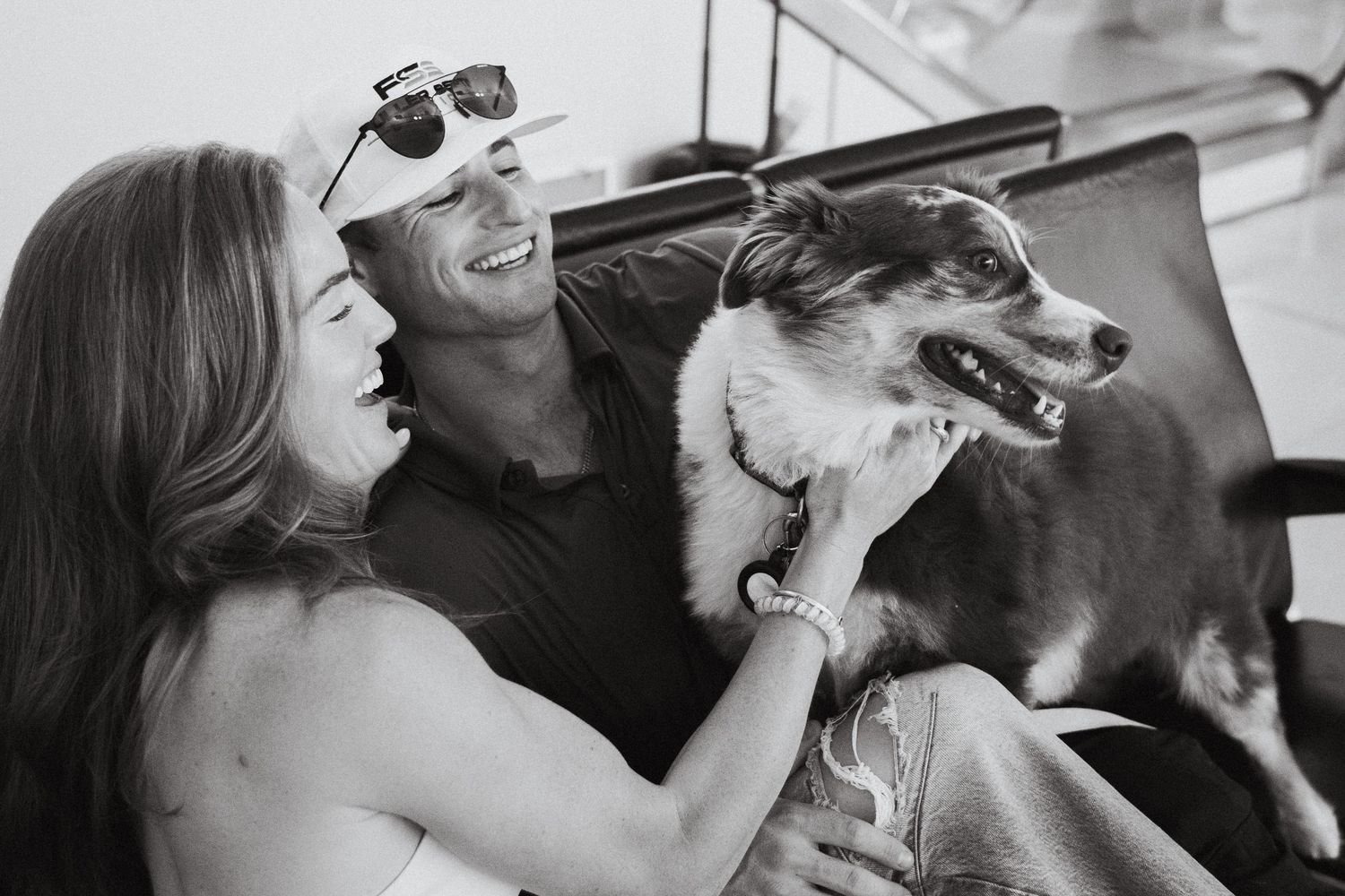 A couple and their dog laughing on an airport bench