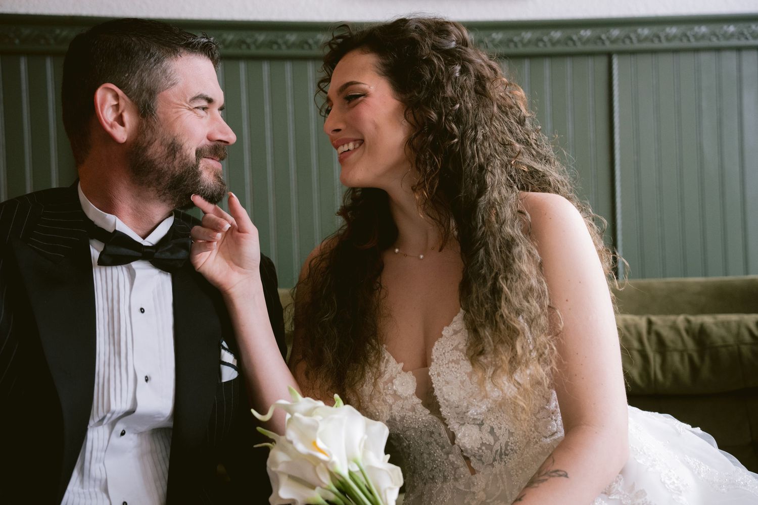 A bride and groom smiling at each other on a velvet couch