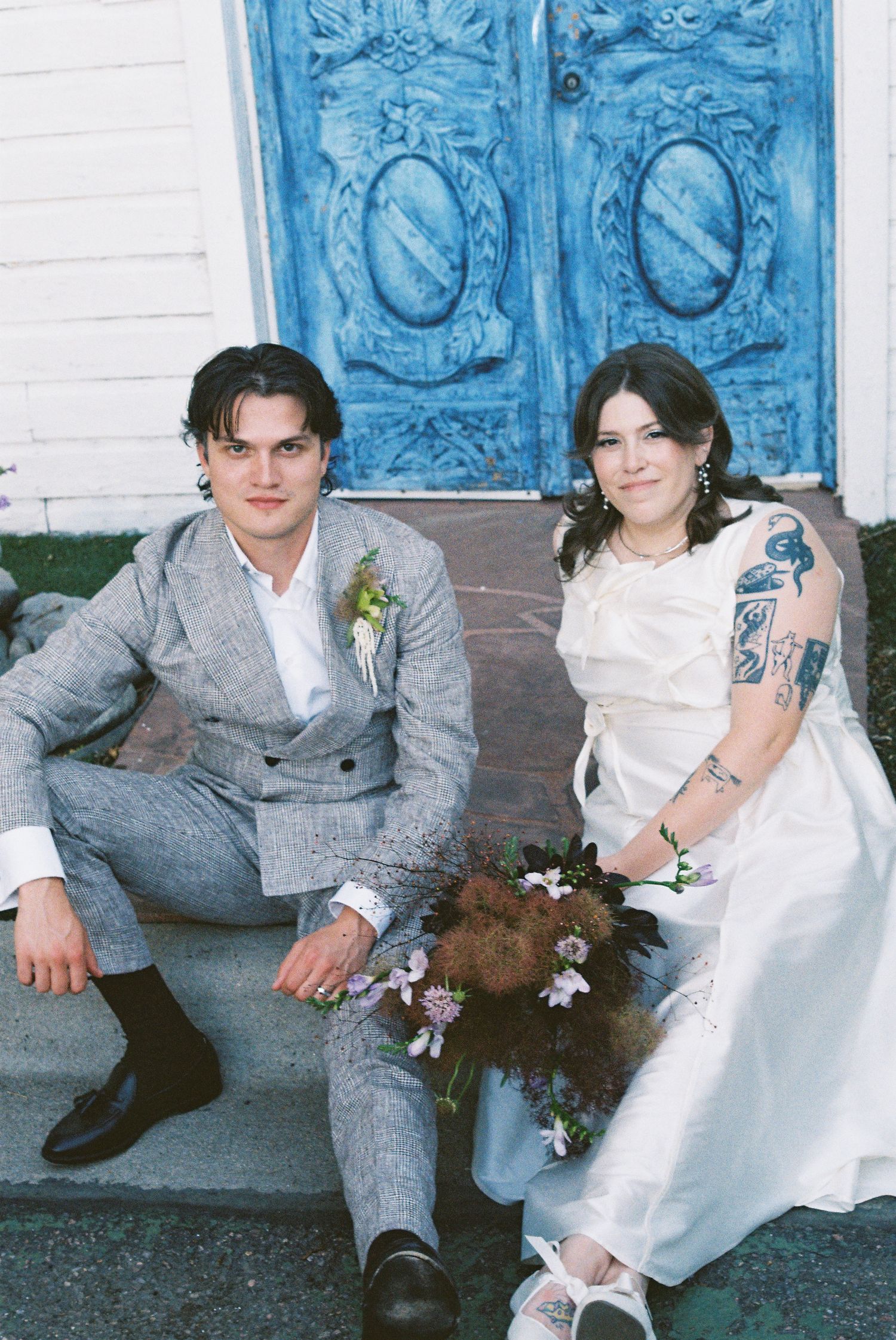A married couple sitting on steps in front of a vibrant blue door