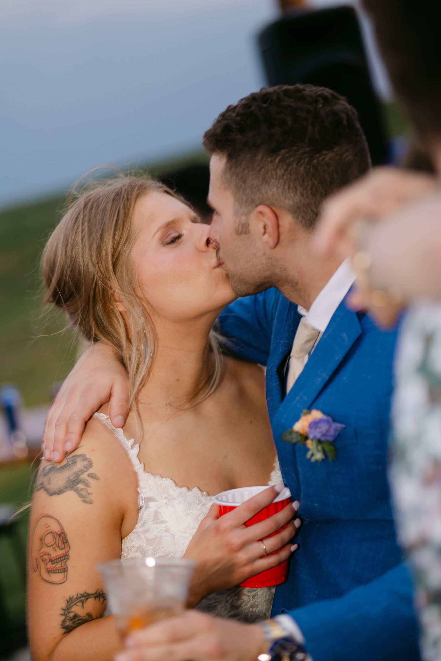 A romantic moment between a couple in formal attire sharing a kiss at an outdoor wedding celebration.