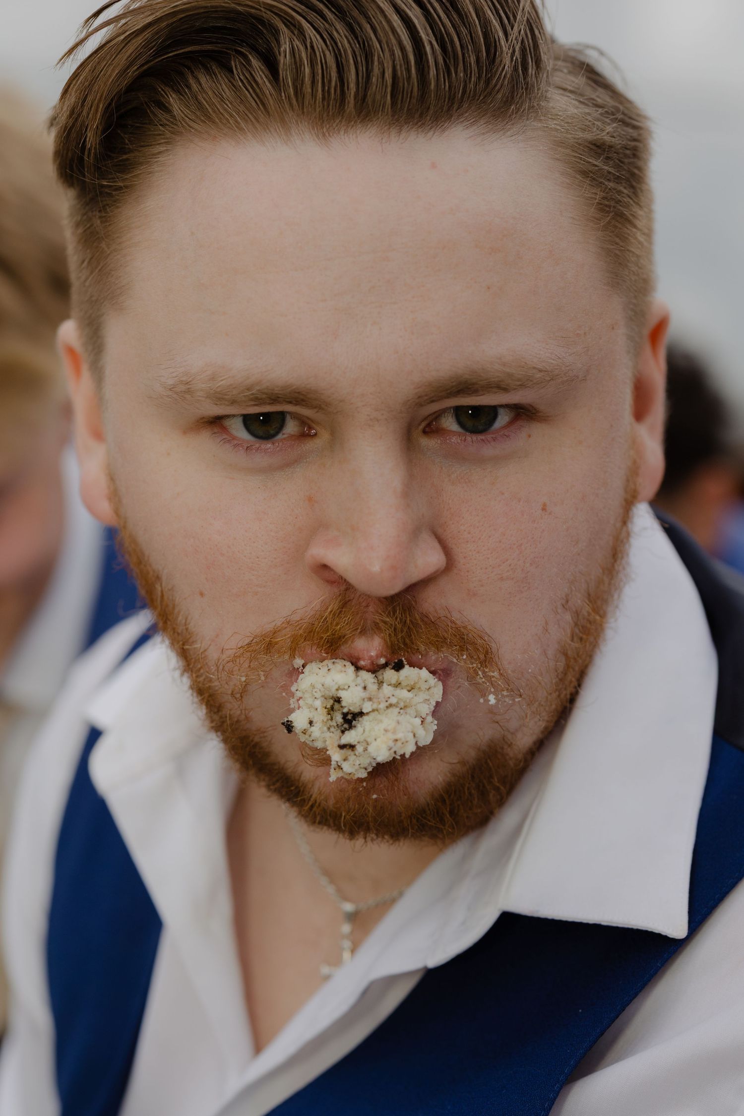 Close-up progression of a man in a navy suit getting cake on his face while eating dessert.