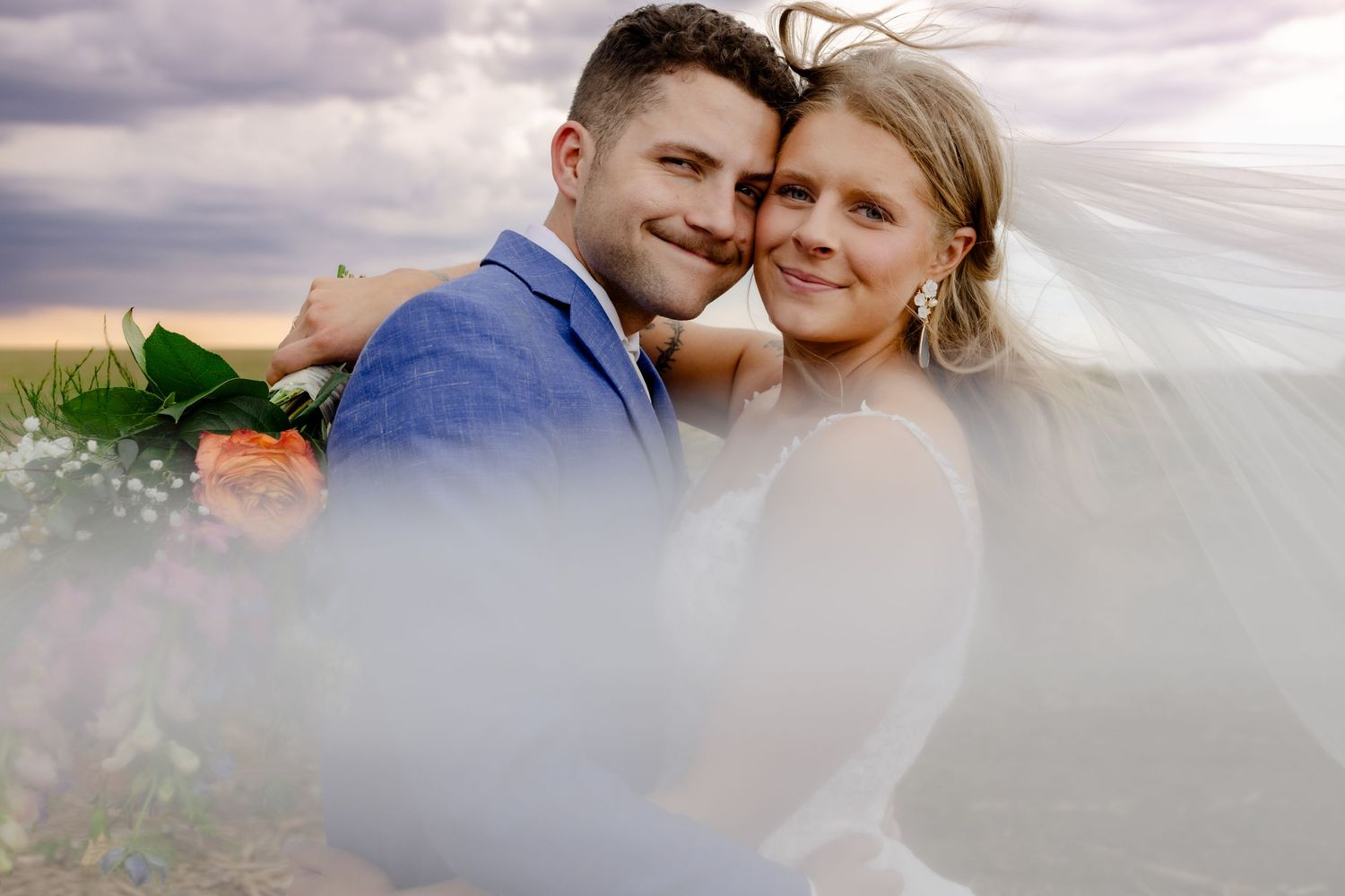 A close-up wedding photo on a cloudy day with soft lighting and ethereal veil movement.