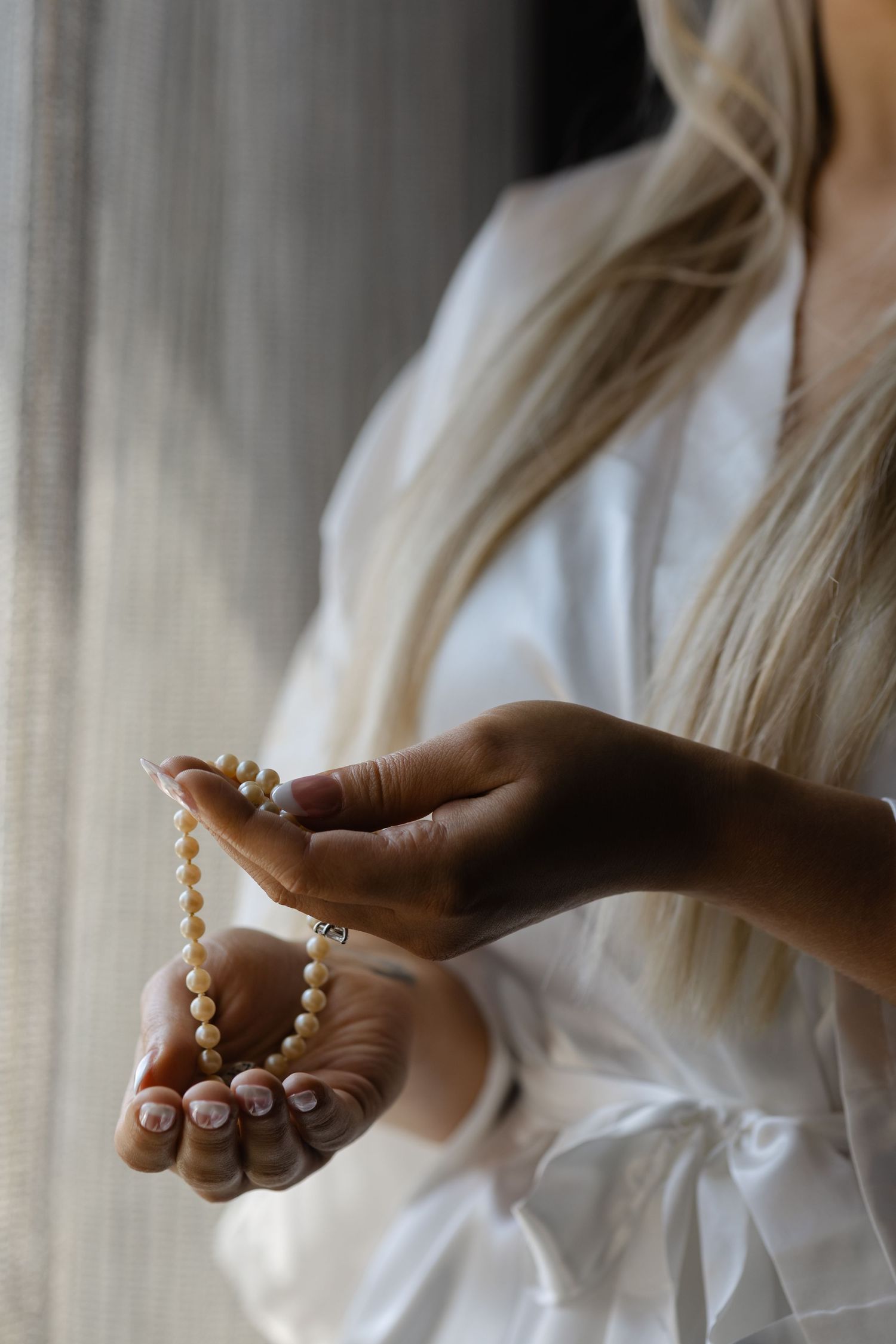 Hands wearing white sleeve holding strings of delicate round beads from right to left in a graceful sequence.