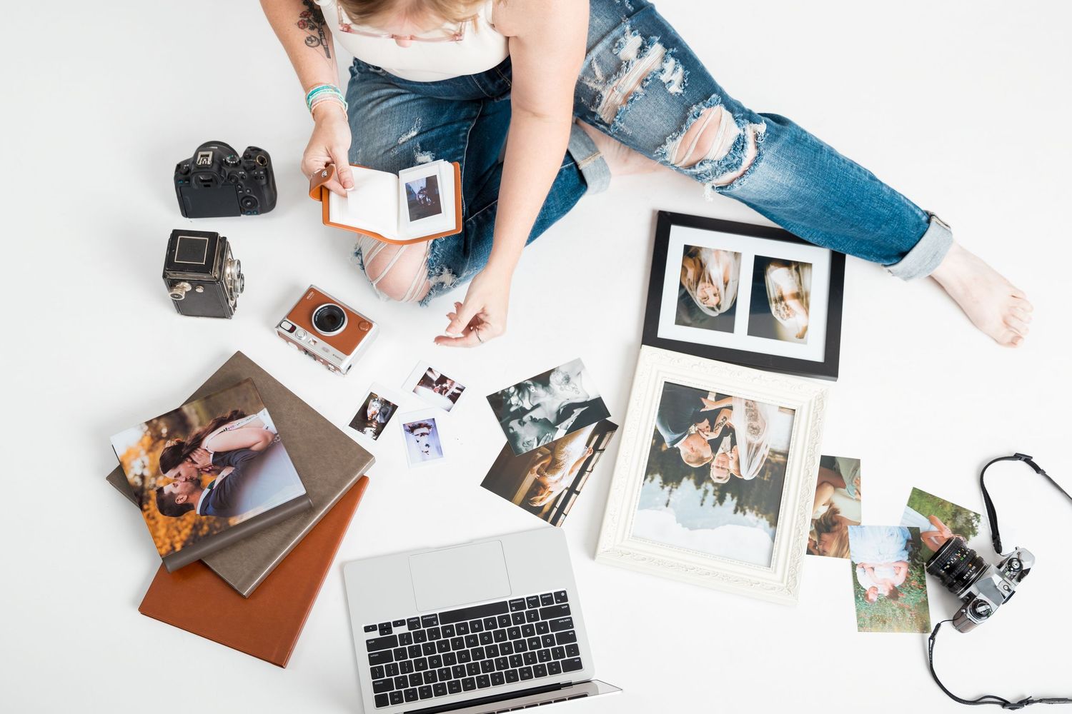Flatlay of office supplies including keyboard, photos, mobile phone, and camera equipment on white surface.