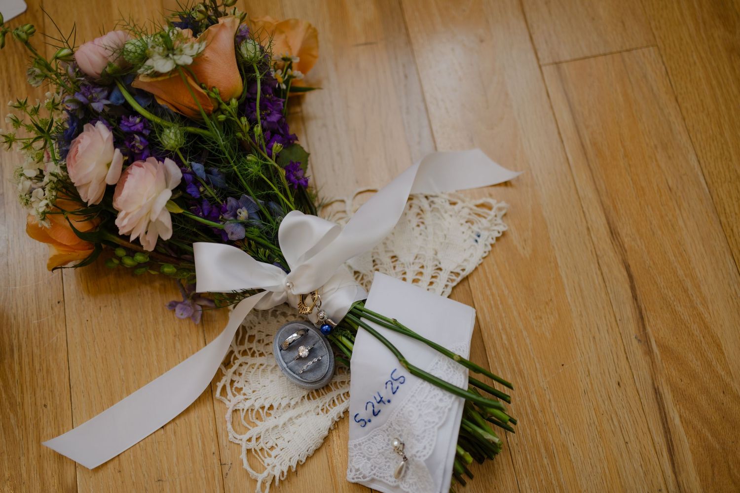 Wedding bouquet with pink and purple flowers wrapped in white lace and ribbon rests on wooden floor. Arbor Hall, Omaha Nebraska