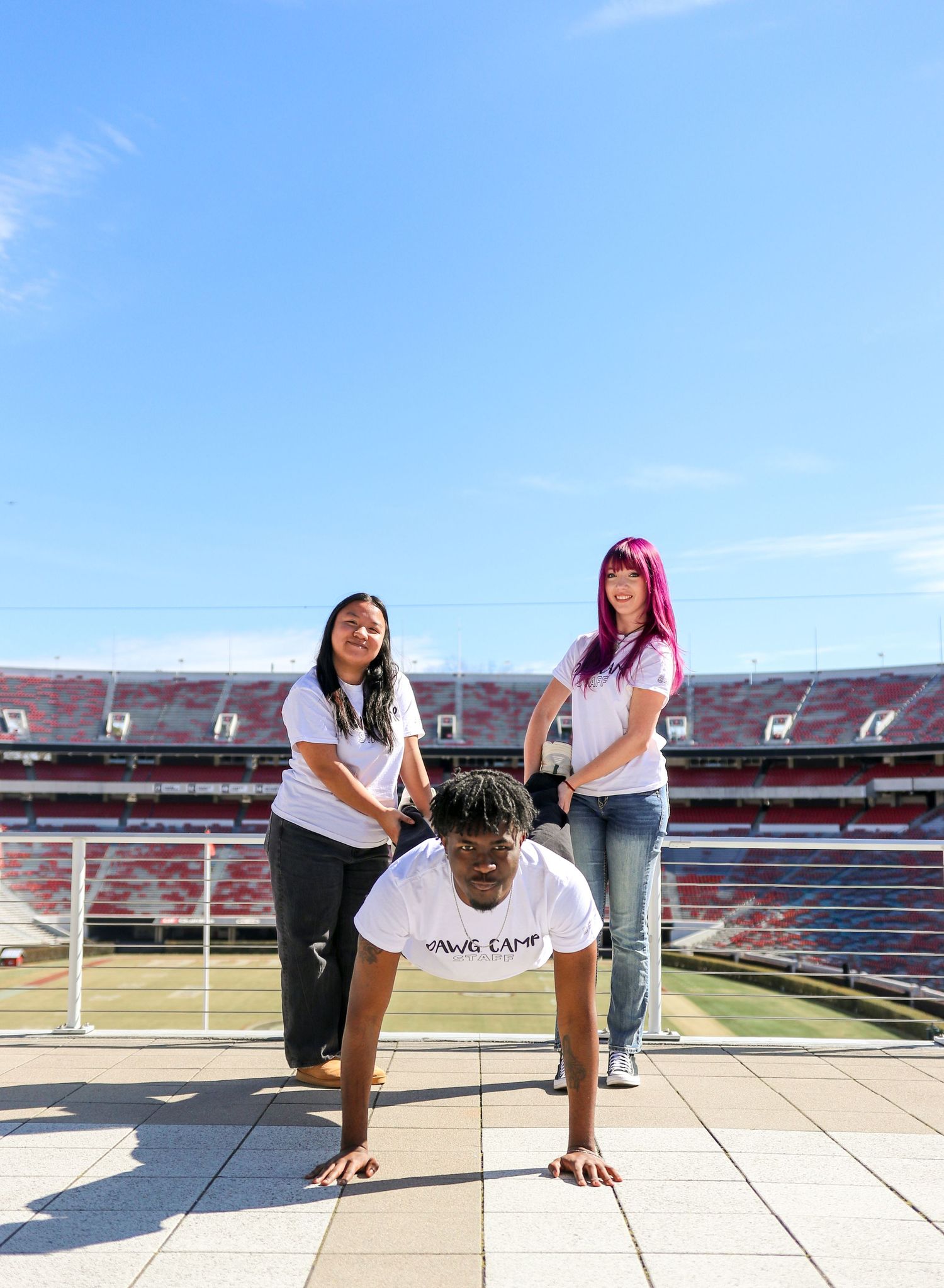 People posing and taking photos in an empty stadium with red seats under blue sky.