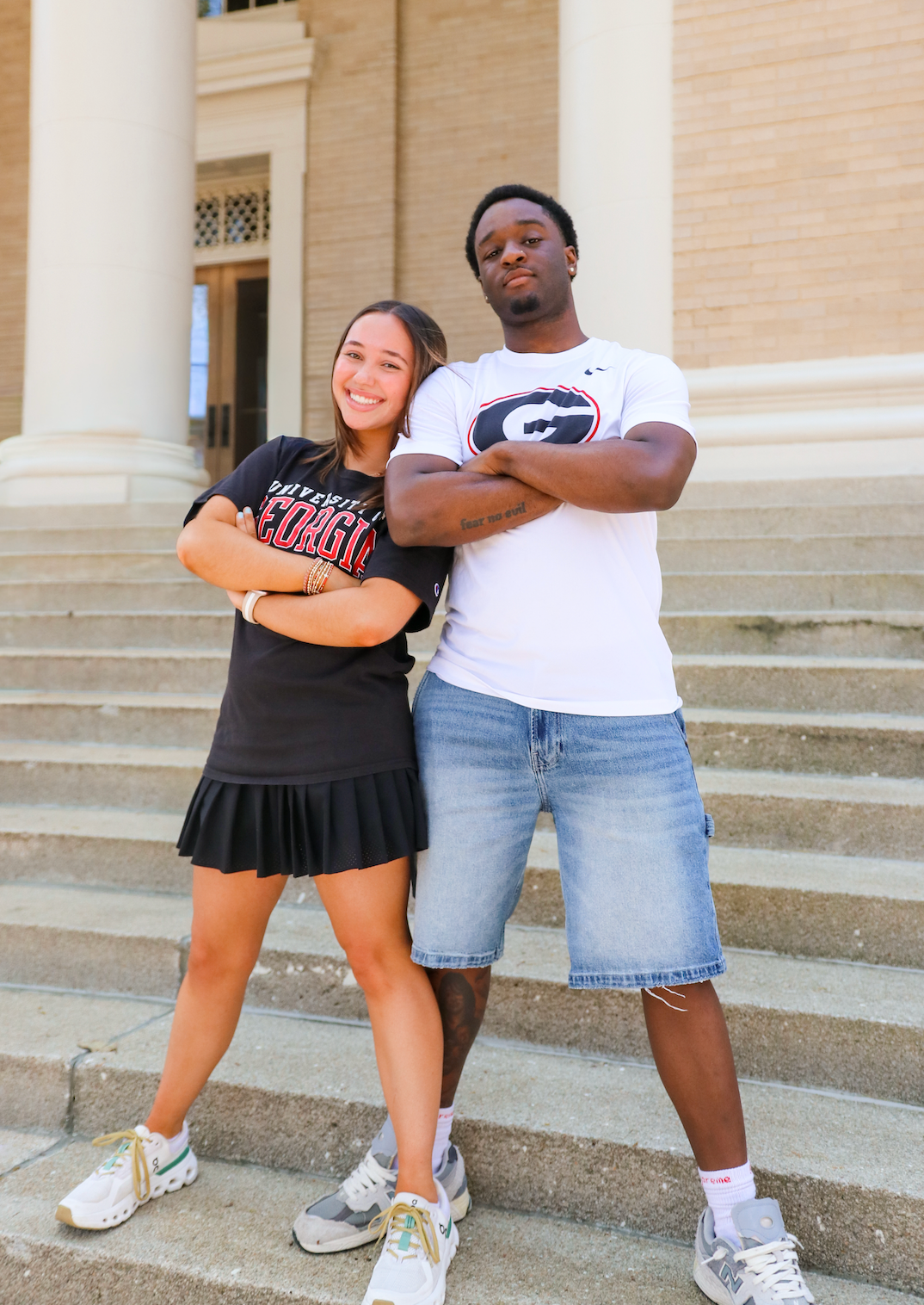 Two college students pose with arms crossed on university steps, wearing Georgia Bulldogs fan apparel.