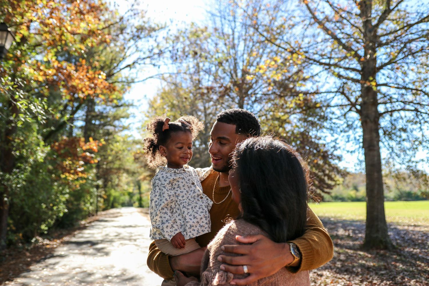 A group of people enjoying a sunny autumn day in a park with golden foliage and trees.