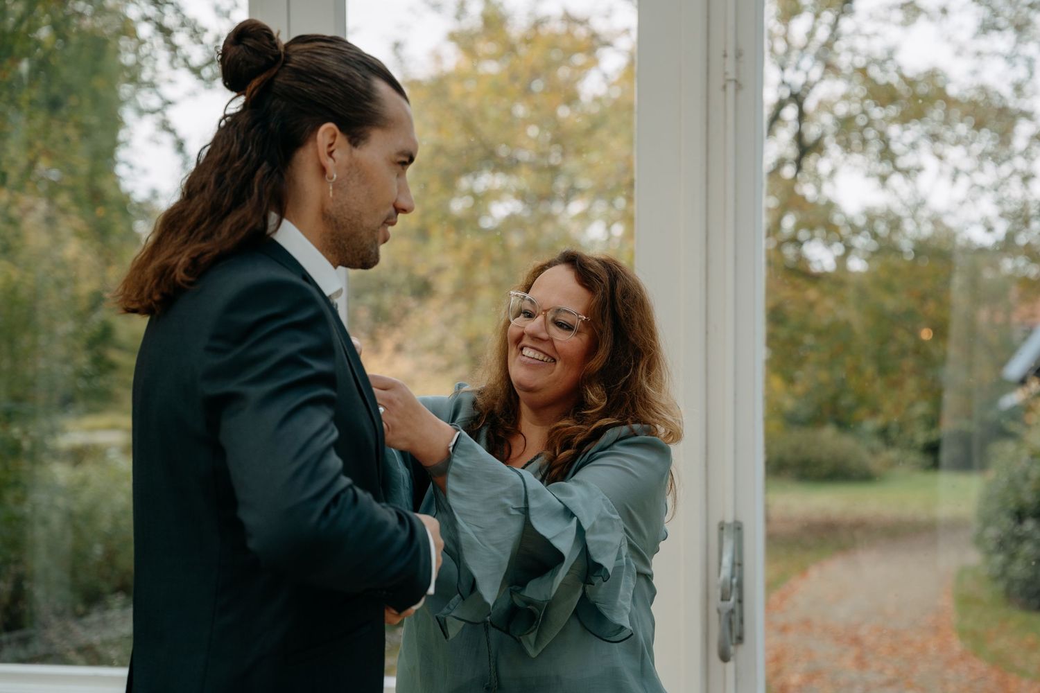 Candid moments captured between couple in elegant glass conservatory with natural lighting.
