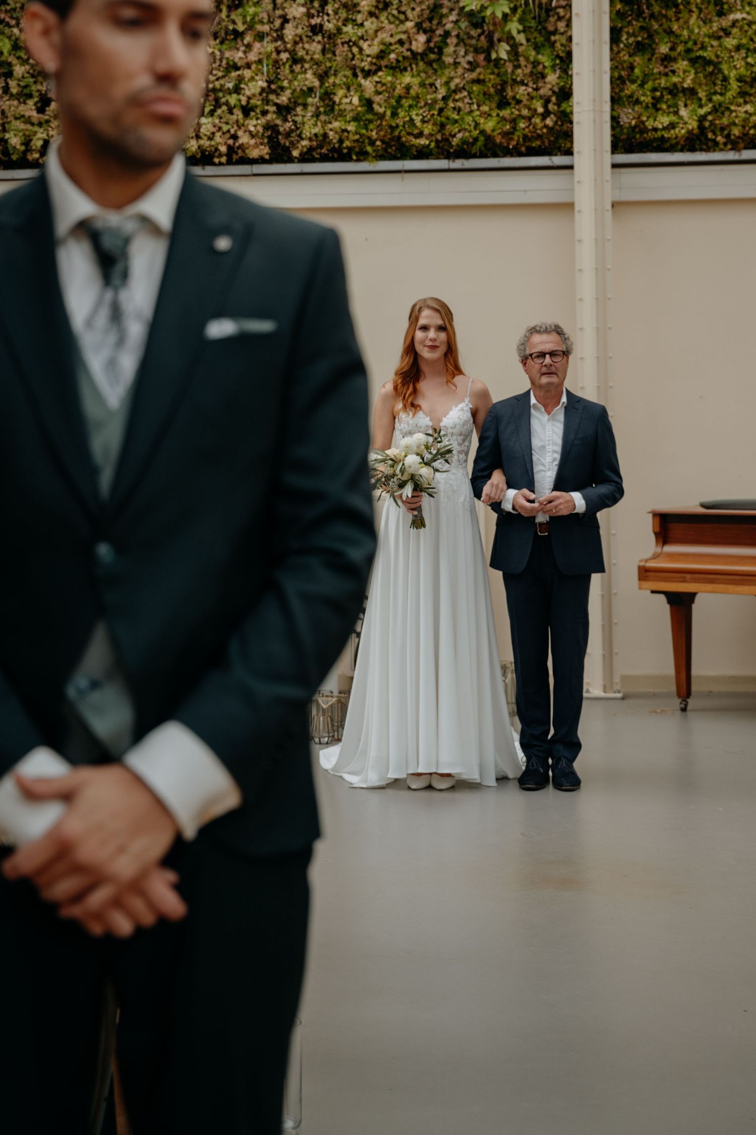 A wedding ceremony scene showing formal attire and a white bridal gown in an indoor venue.