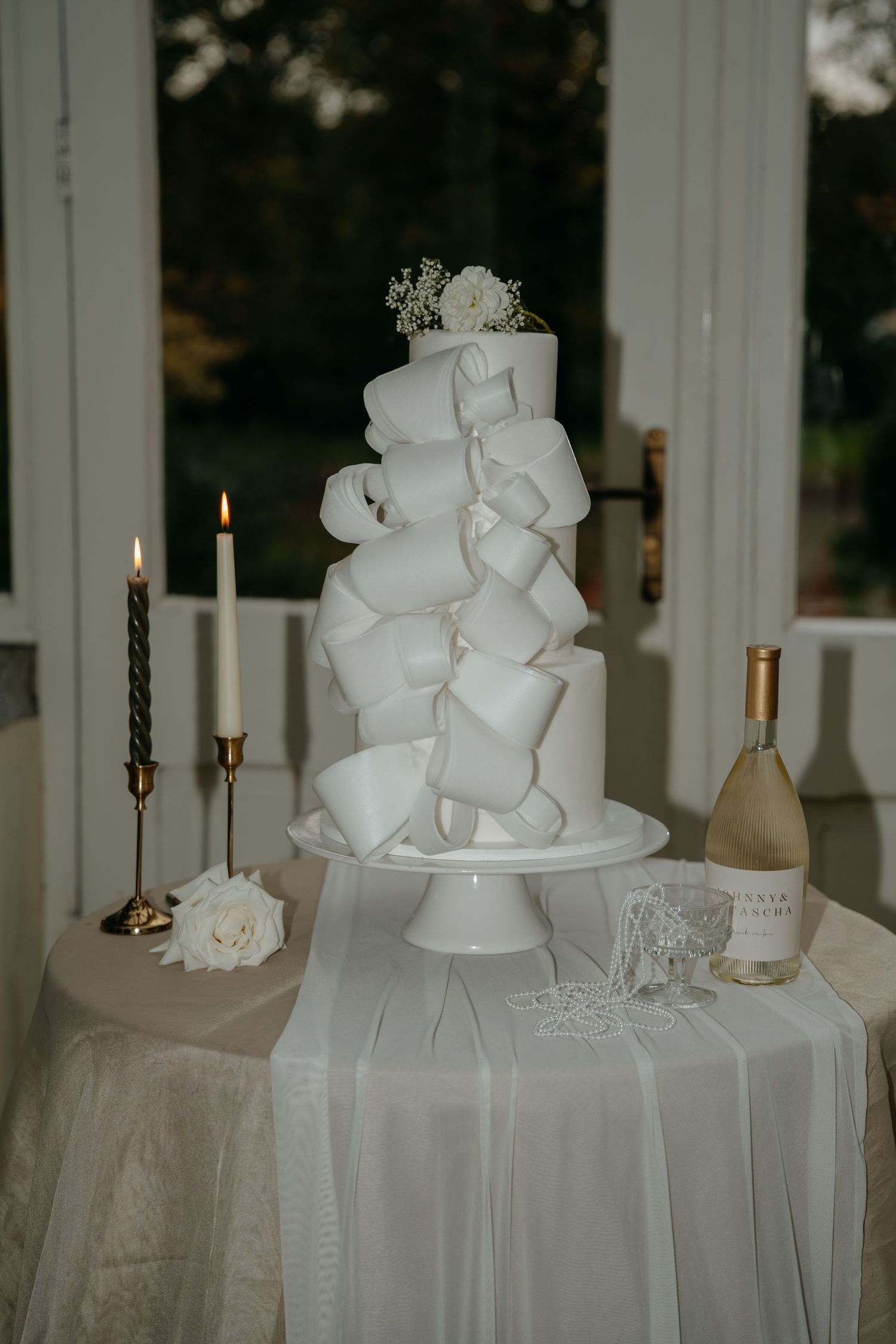 Modern white wedding cake with geometric bow details displayed with candles and champagne.