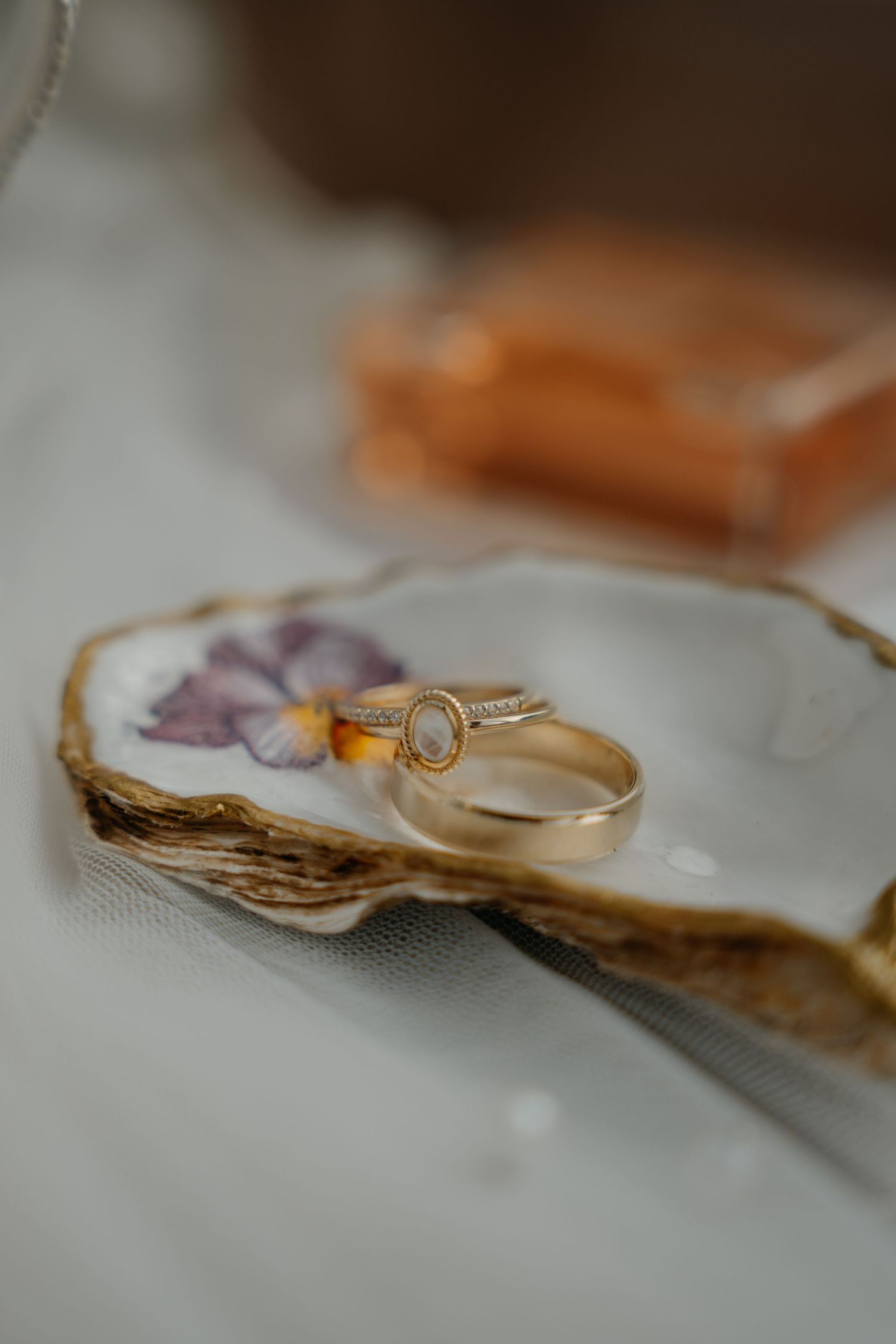 Two gold wedding rings resting on a decorative oyster shell dish with a floral design.
