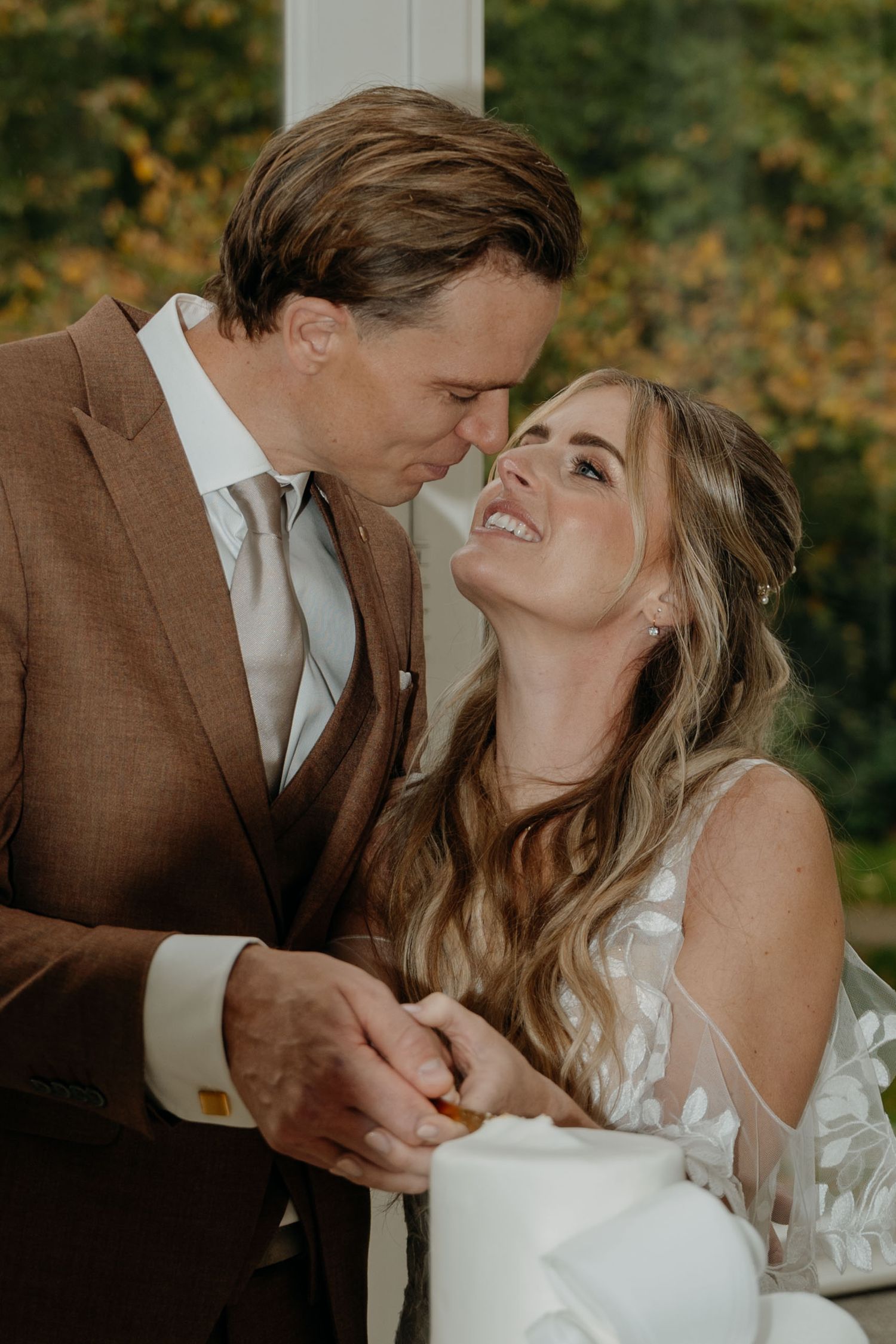 Intimate moment between newlyweds sharing laughter by their wedding cake display.