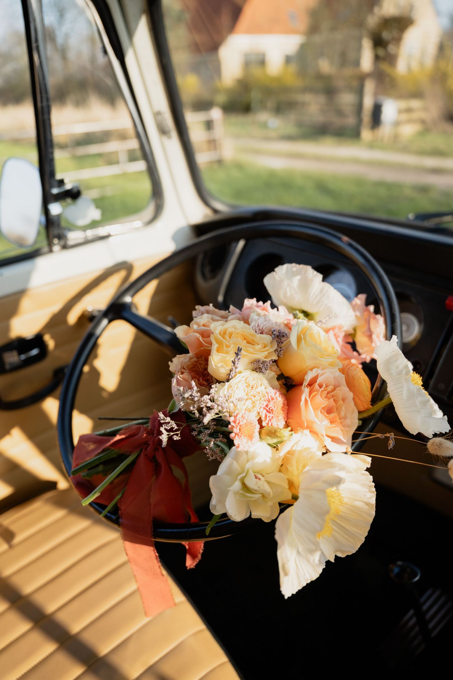 A bridal bouquet of peach roses and white flowers resting on the dashboard of a vintage vehicle.