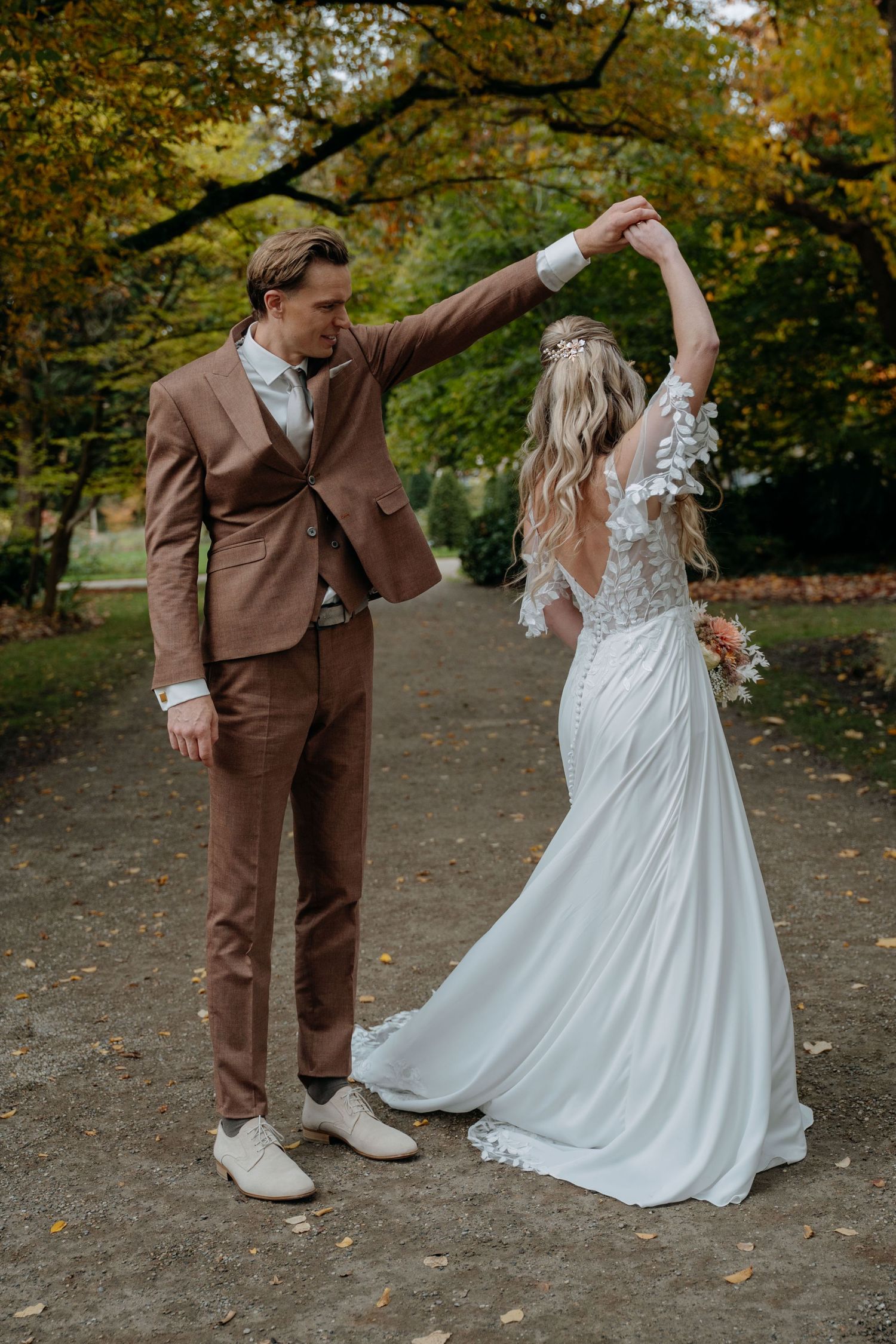 A couple in wedding attire dancing together on an autumn day with fall foliage in the background.