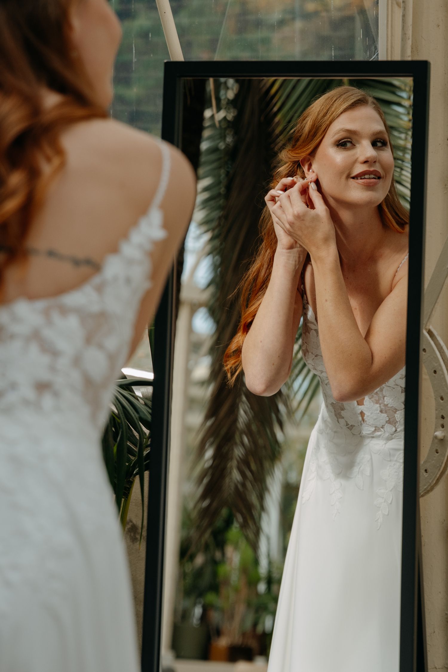 Bride getting ready in front of a mirror with tropical plants in the background.