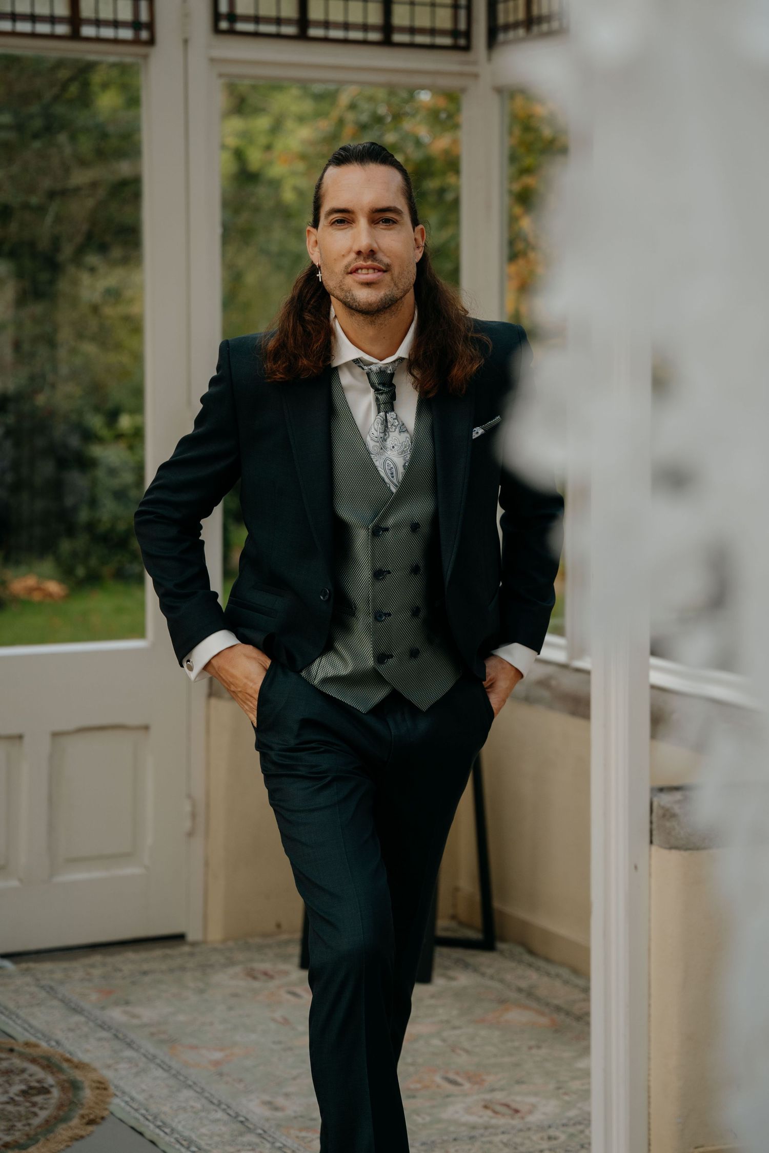 A formal portrait series showing someone in a classic black suit and vest posing on a white porch in natural lighting.