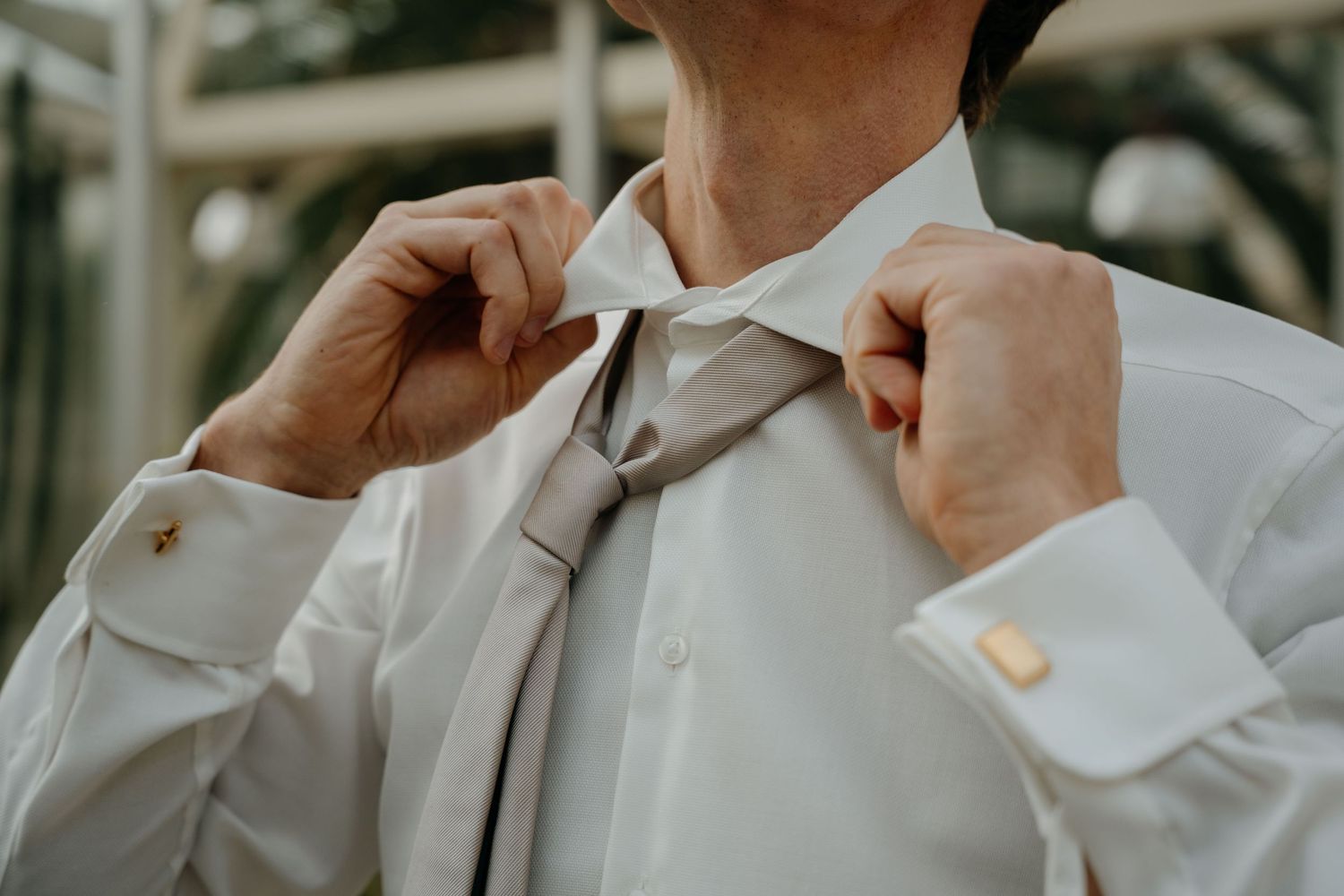 A group of groomsmen in light gray suits adjust their bow ties and collars while getting ready.