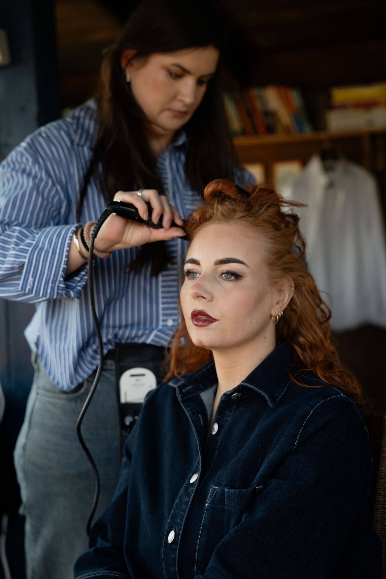 A hairstylist curling a redhead woman's hair with a curling iron in a salon setting.