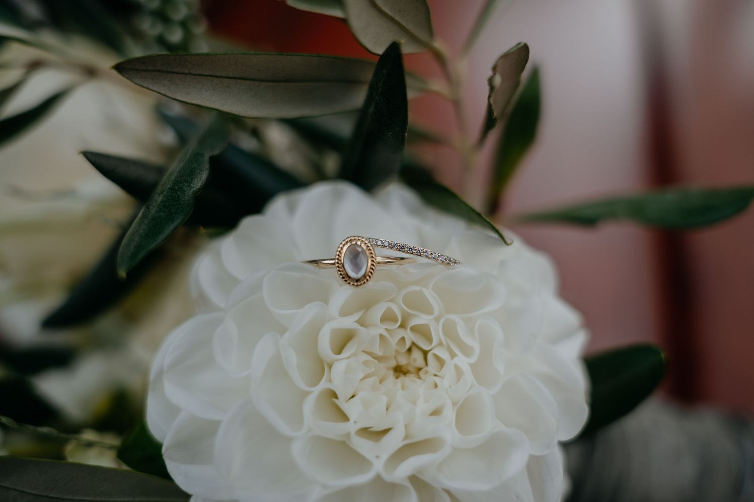 Close-up detail of a white dahlia flower with an engagement ring nestled among its petals.