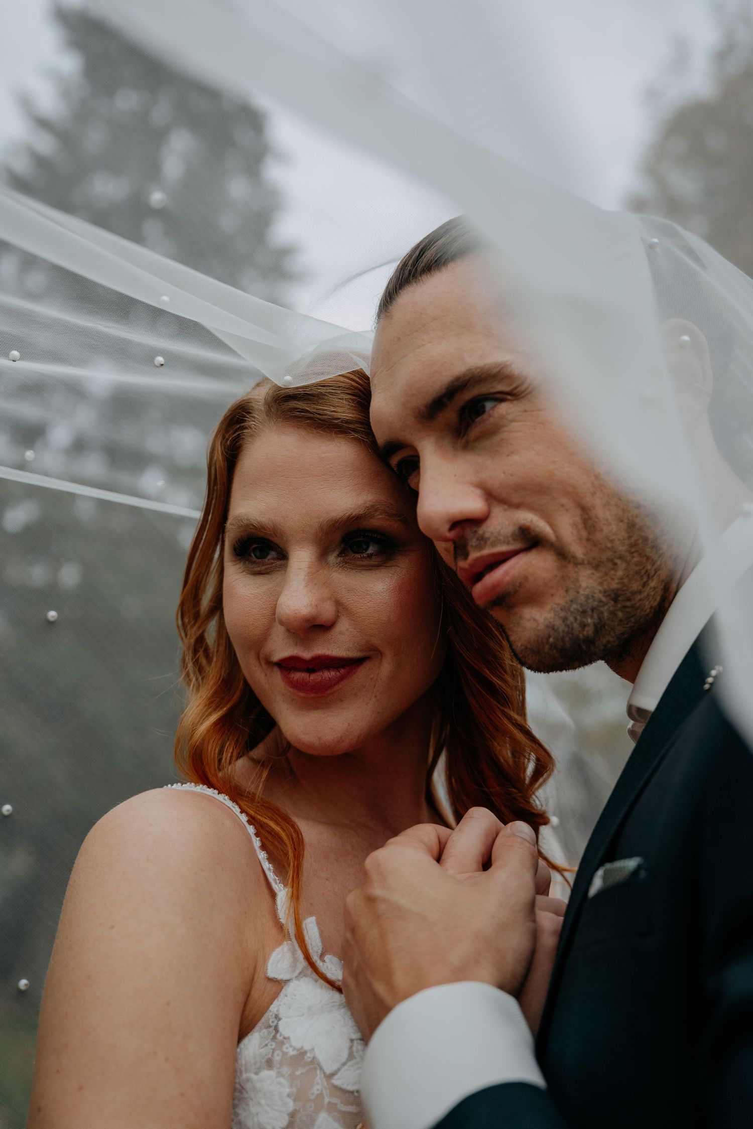 A romantic wedding portrait showing an intimate moment between newlyweds against a misty outdoor background.