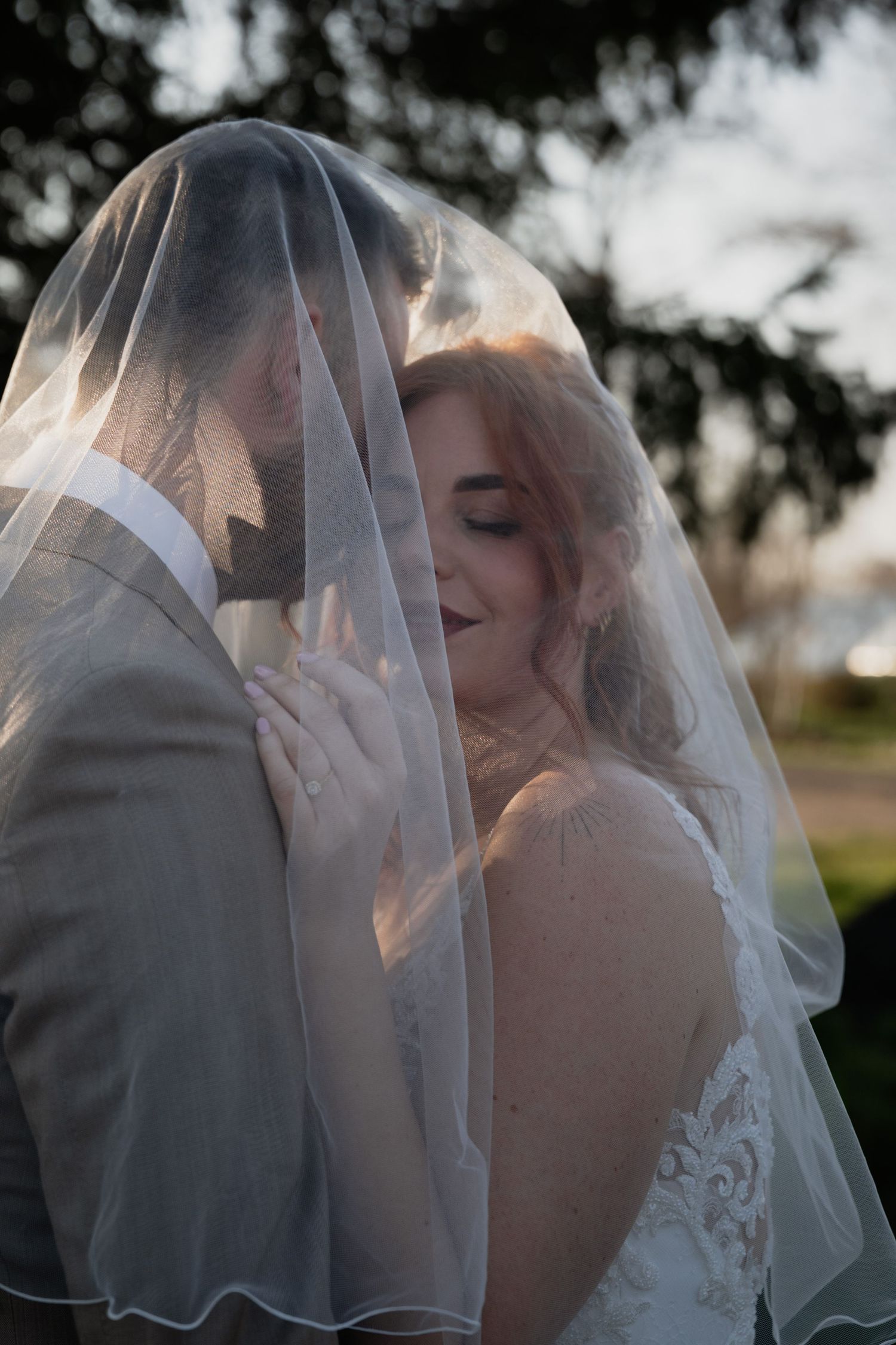 Bride and groom sharing an intimate moment under a sheer wedding veil, bride smiling with eyes closed in bridal gown.