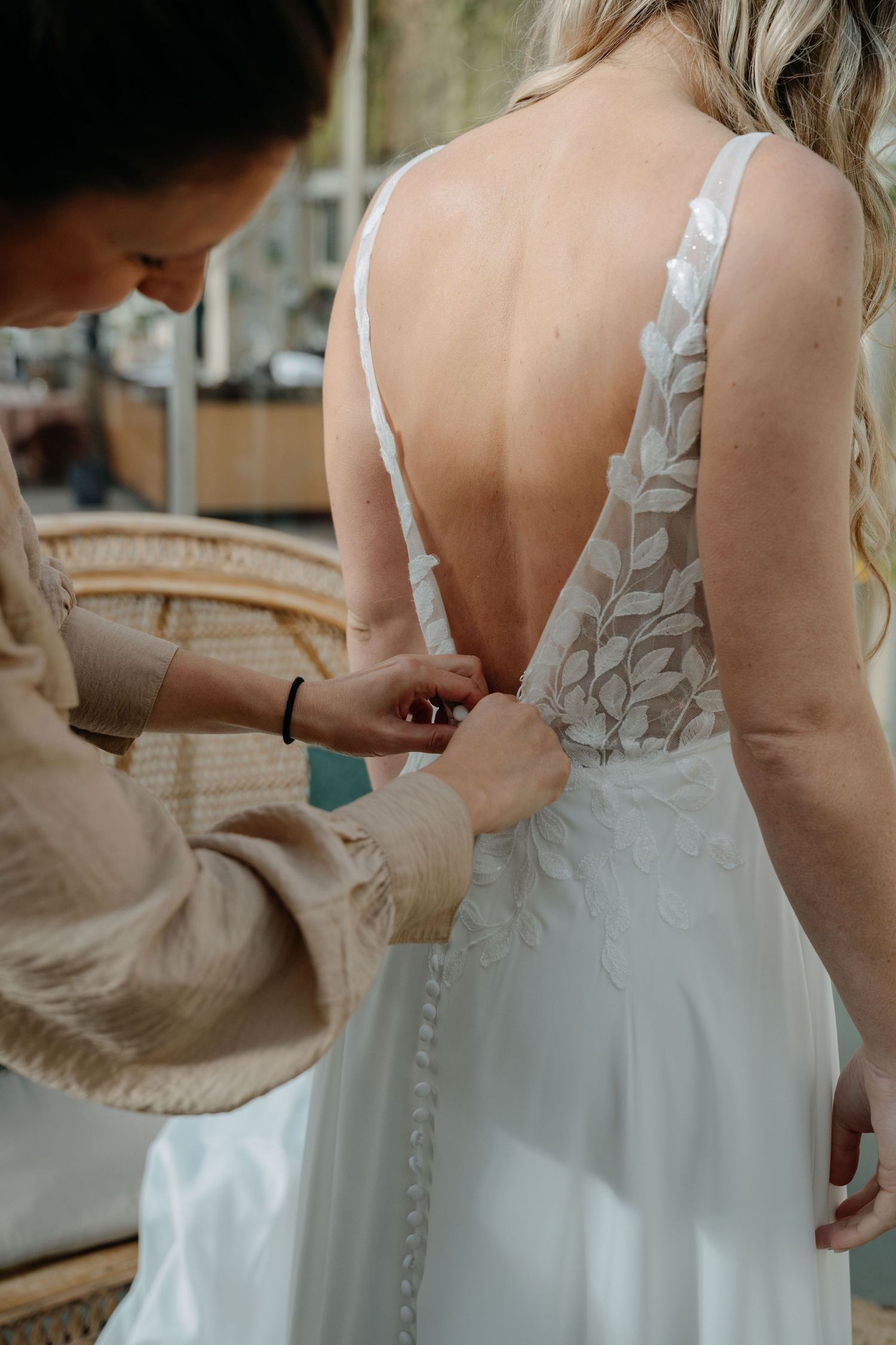 Close-up sequence of someone fastening delicate pearl buttons on the back of an elegant white wedding dress.