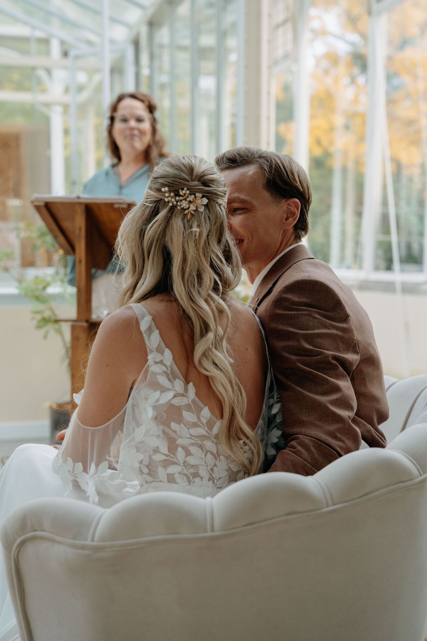 A bride and groom share a joyful moment during their wedding ceremony in a sunlit greenhouse venue.