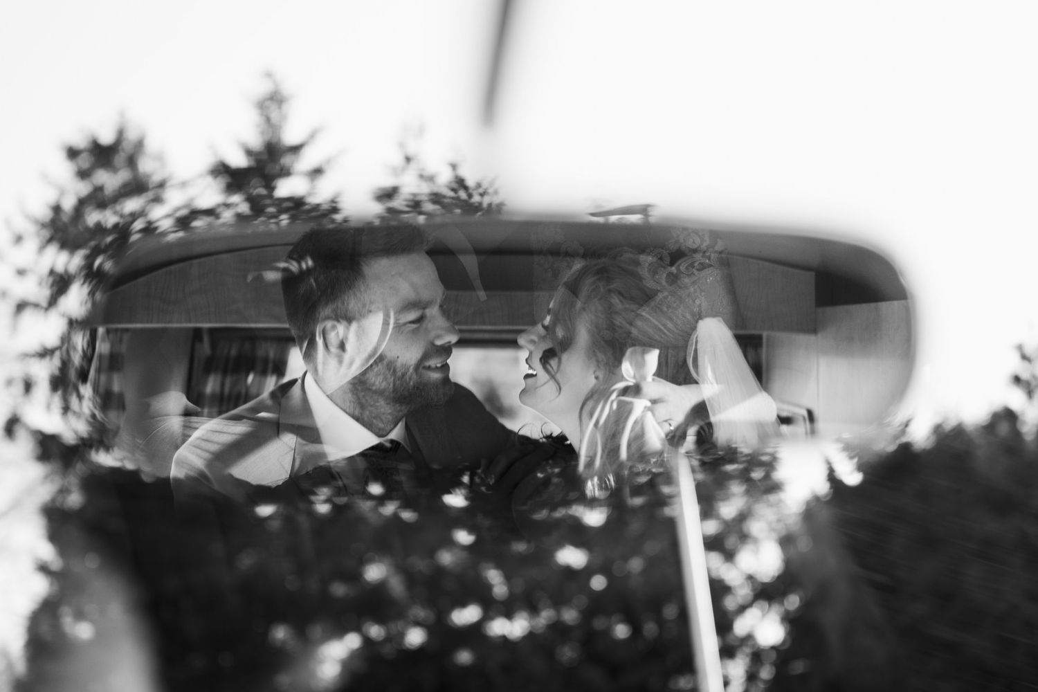 Black and white photo of a smiling couple sharing a romantic moment inside a vintage car.