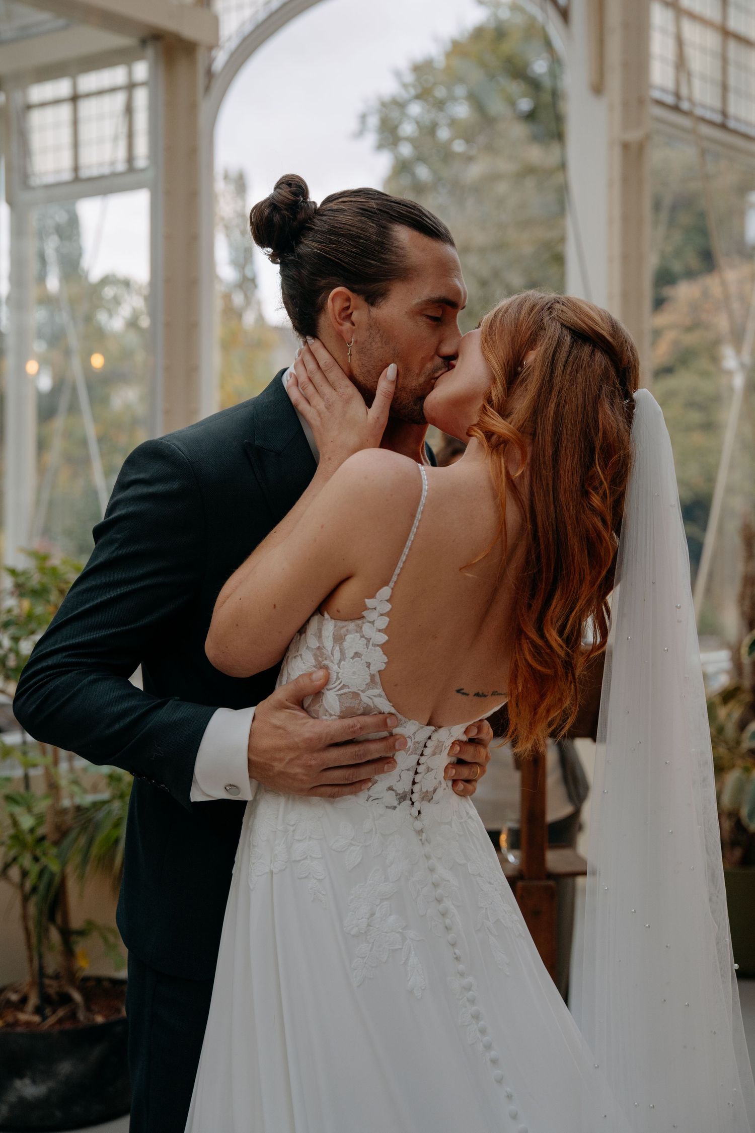 Romantic wedding couple embracing in an elegant glass conservatory setting.