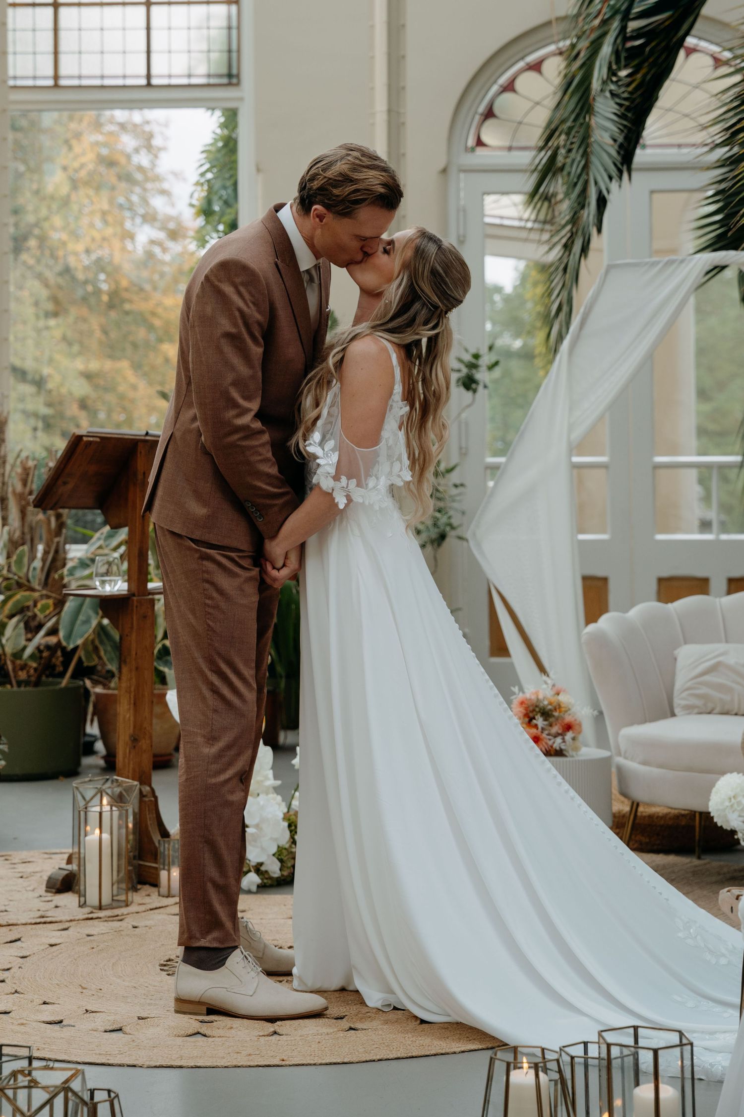 A romantic first look moment between a bride in white and groom in brown at an elegant indoor venue with large windows.