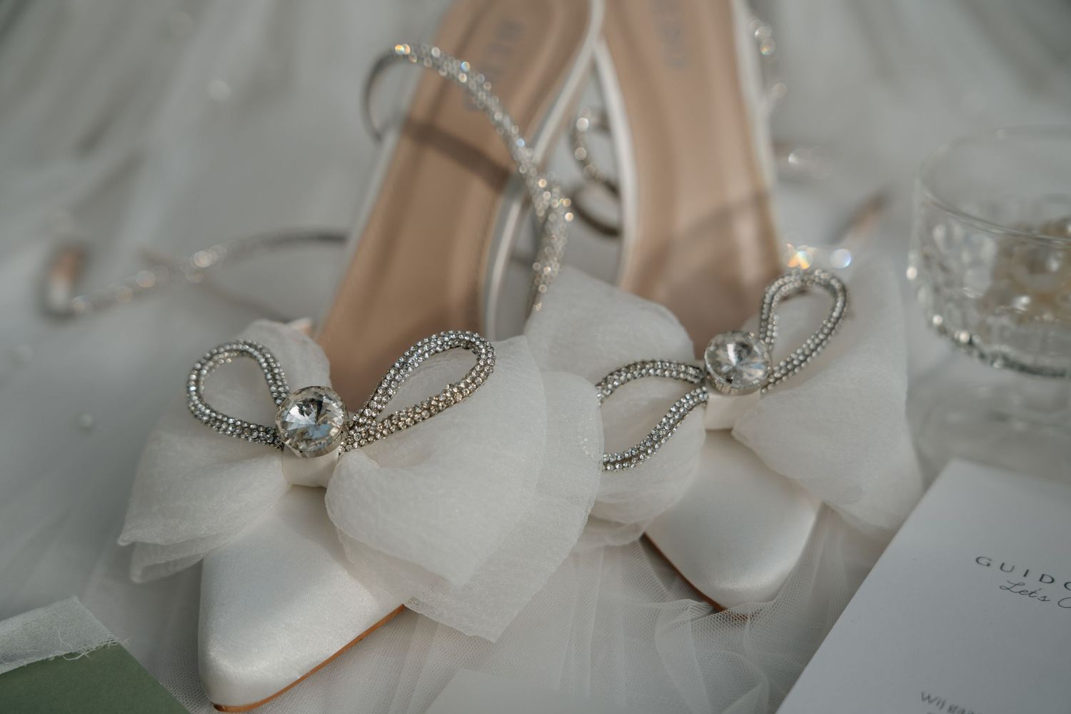 A series of elegant white bridal shoes and delicate jewelry arranged in a soft, romantic composition.