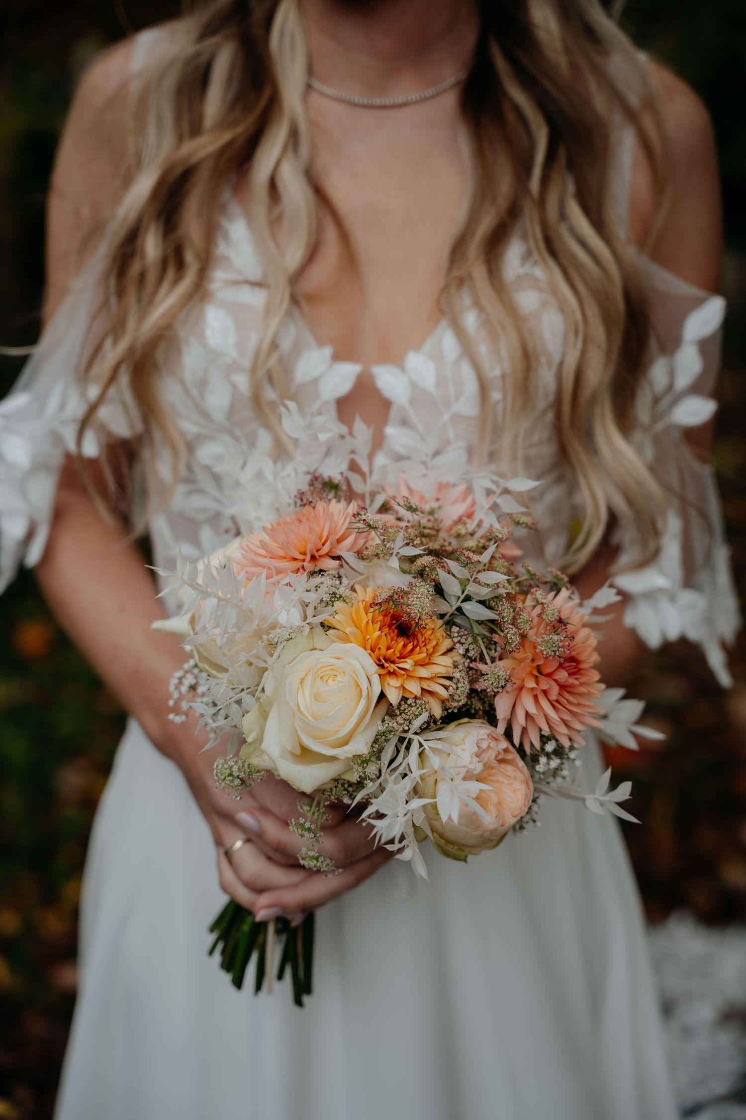Close-up of a bridal bouquet with peach dahlias, white roses and delicate lace details on the dress.