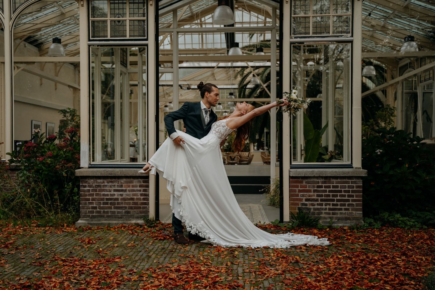 Elegant greenhouse wedding venue with white pillars and autumn leaves scattered on the ground.