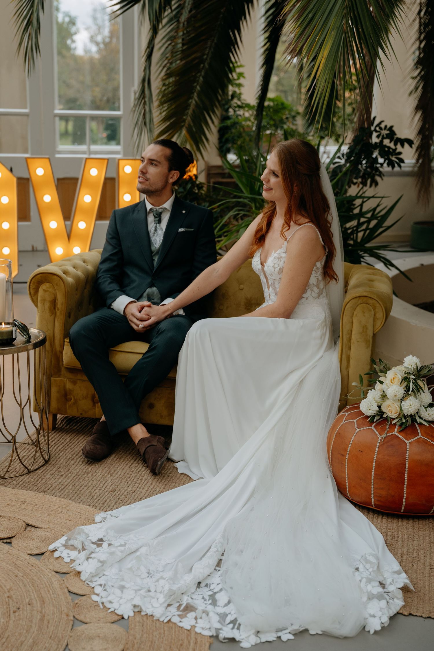 Wedding couple relaxing on vintage furniture with decorative lights in background.