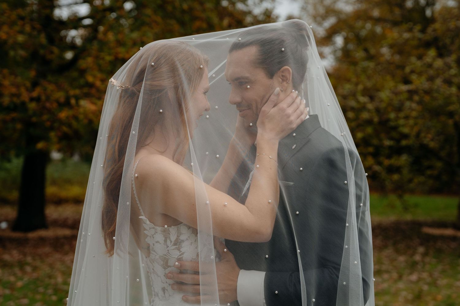 Bride and groom sharing a romantic moment under a wedding veil outdoors in autumn.