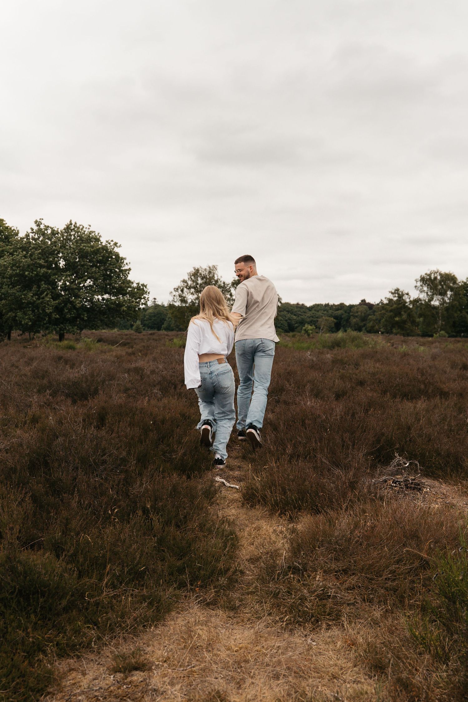 Een verliefd stel dat lachend over de paarse heide in Laren rent in het zachte lentelicht.